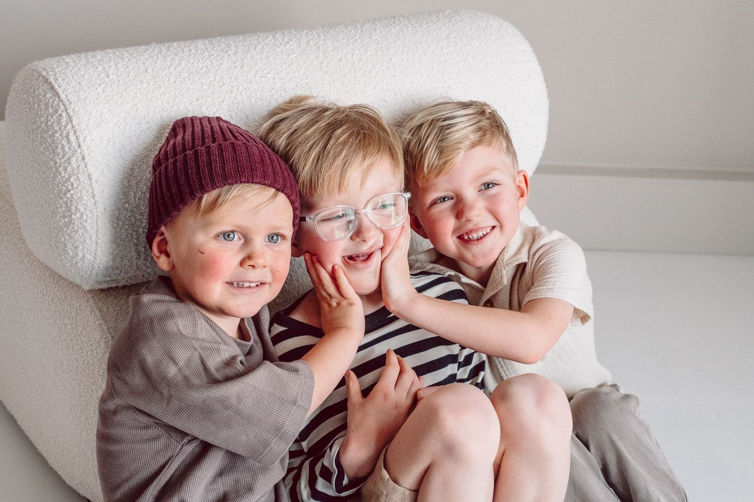 Tre bröder sitter på golvet i fotostudio. Dom lutar sig mot en vit fåtölj. En har glasögon och en har mössa. Dom busar.