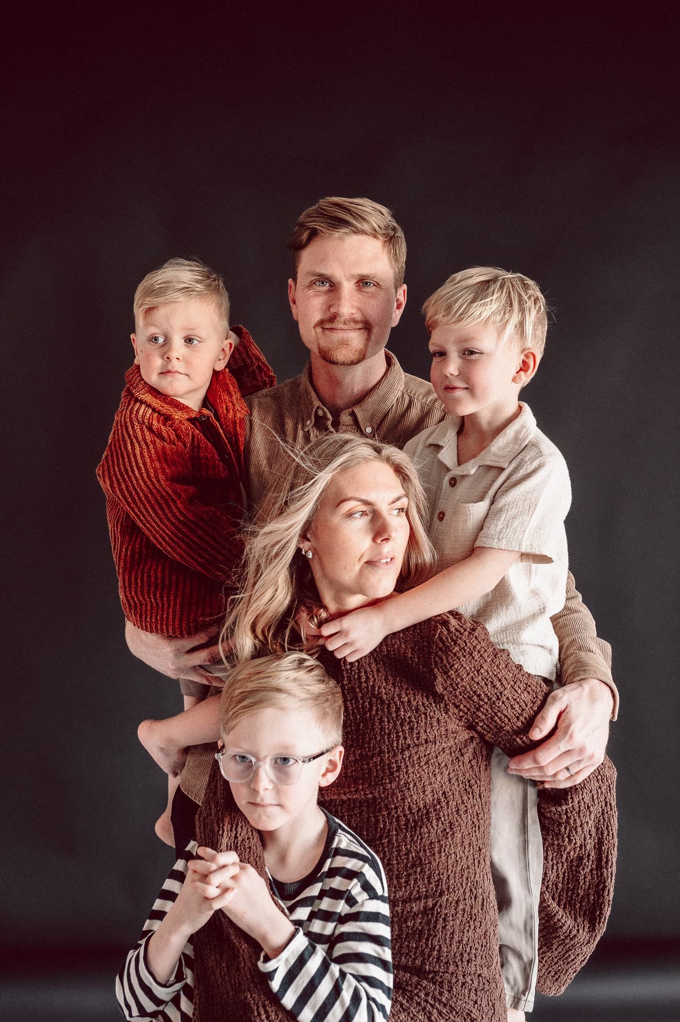 Familj med 3 barn håller om varandra under en familjefotografering i studio i Mullsjö - Jönköping. Mamman har brun klänning.