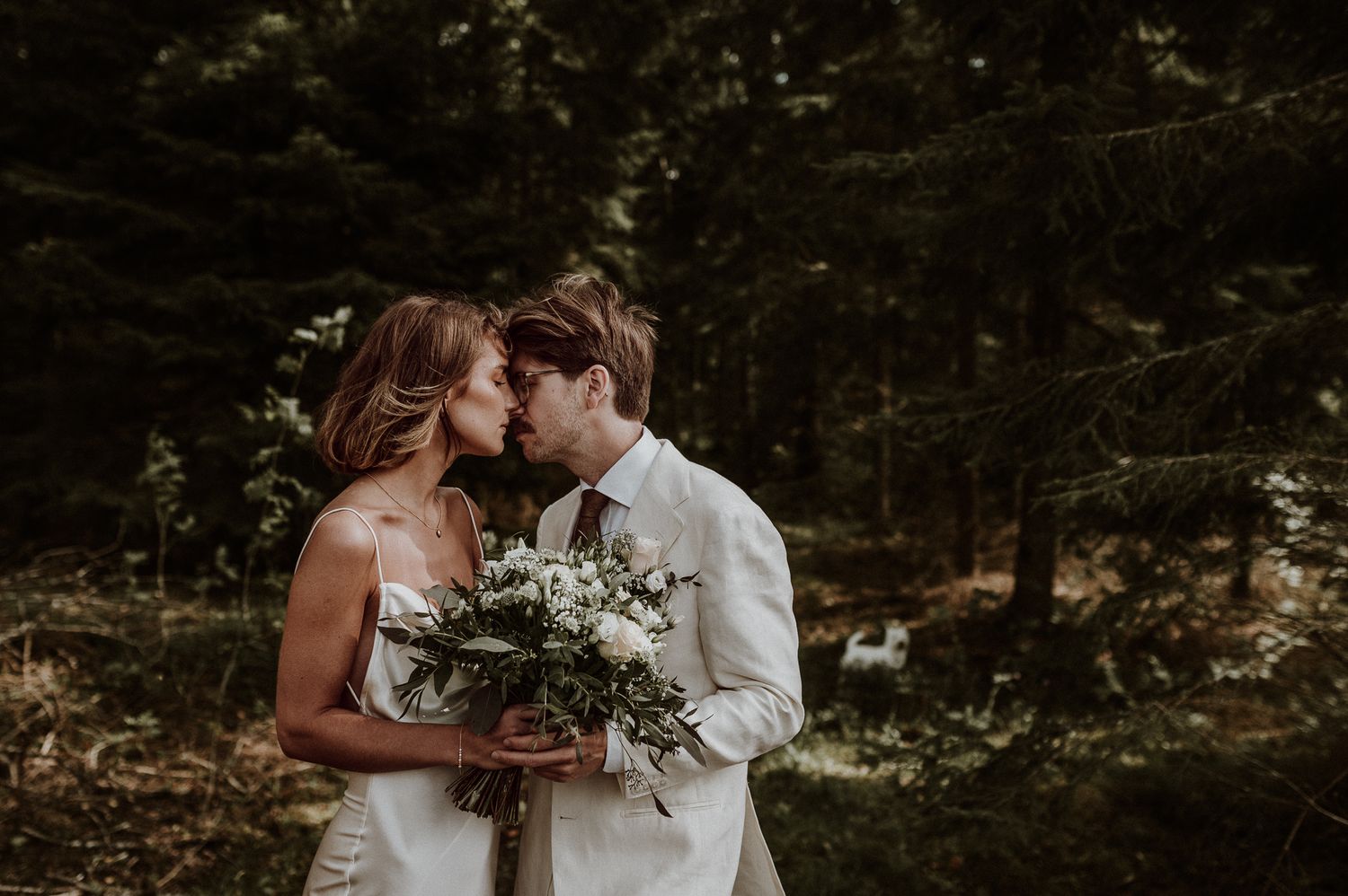 Brudpar med vita kläder lägger pannorna mot varandra under en fotografering med Fotograf Veronica Eng i Mullsjö. Dom håller en brudbukett.