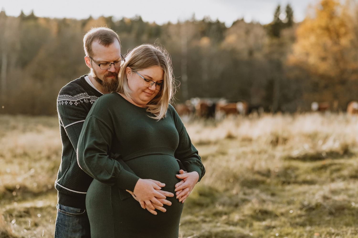 Gravid kvinna står med sin man och håller om gravidmagen. Kvinnan har grön klänning och mannen en stickad tröja.
