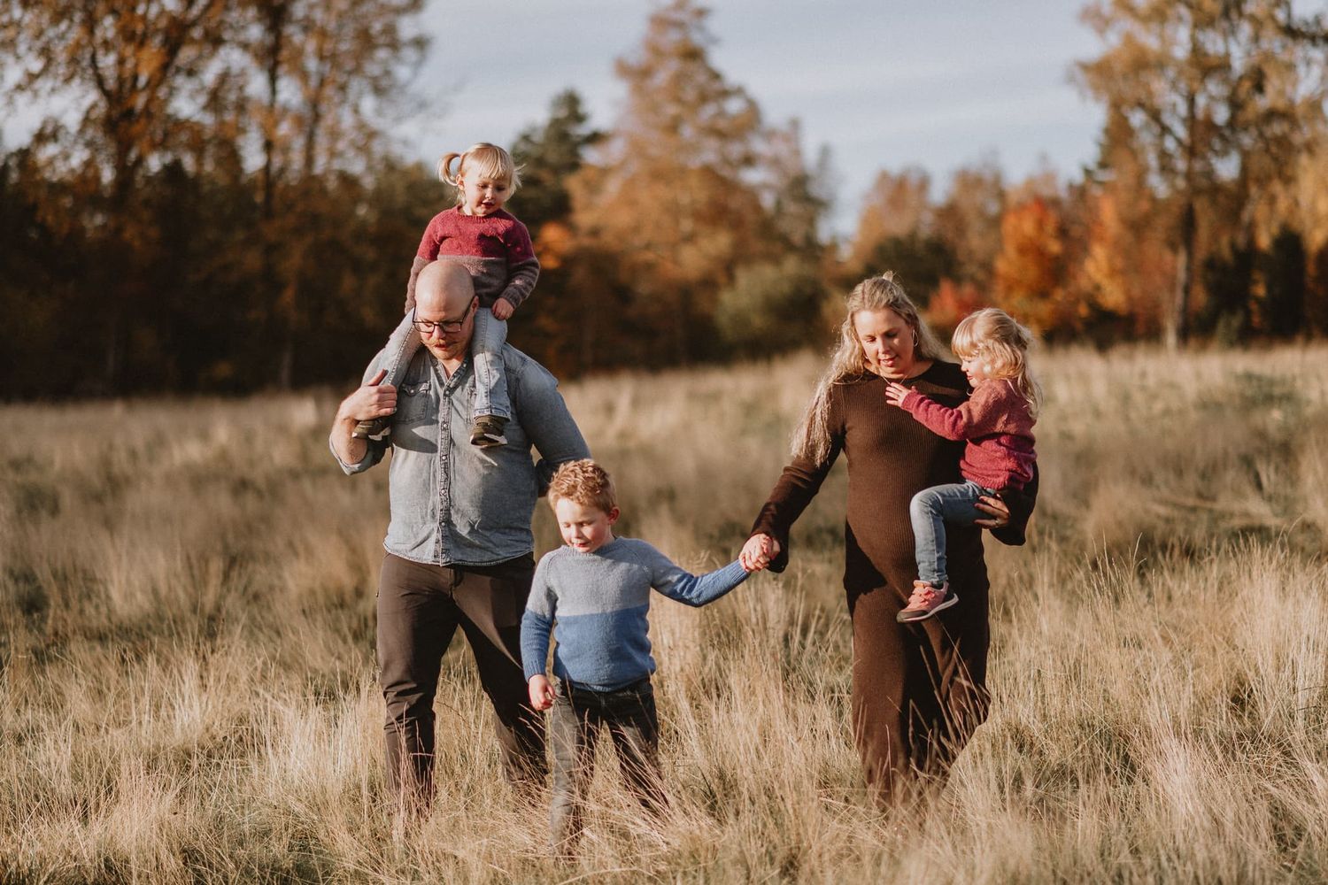 Familj går på en äng vid Näs Herrgård under en familjefotografering. Barnen har stickade tröjor.