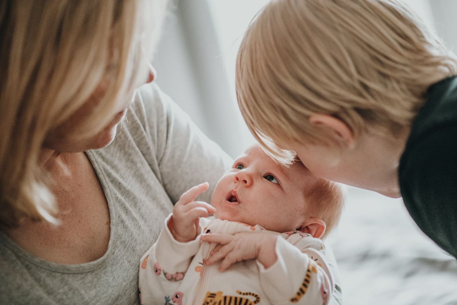 Mamma håller sin bebis i famnen, och storebror lutar sitt huvud mot bebisens.