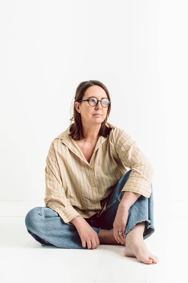 Veronica Eng sitter på golvet i sin fotostudio. Hon har en beige skjorta och jeans. Hon har svarta runda glasögon på sig.