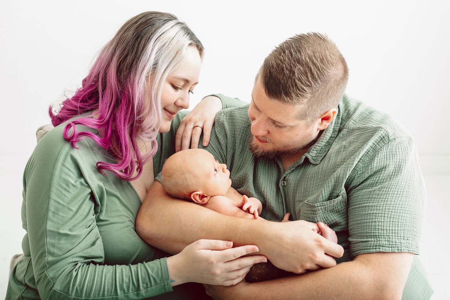 Familj med nyfödd pojke fotograferas i studio i Mullsjö/Jönköping. Föräldrarna har gröna kläder och mamman har rosa hår.