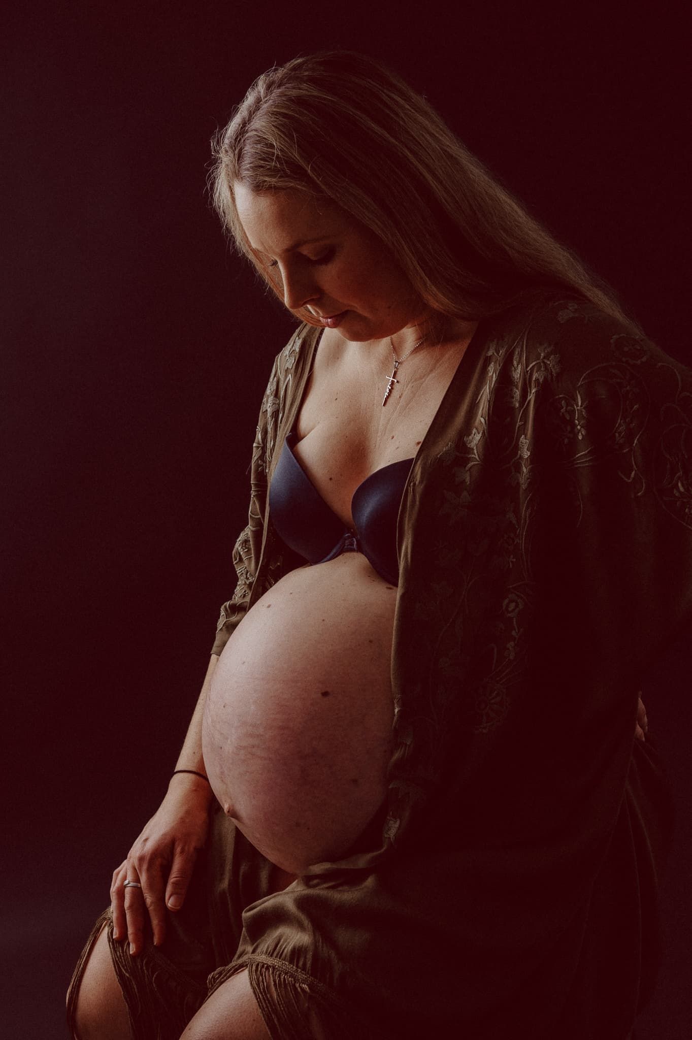 Gravid kvinna med bh och kaftan tittar ner över sin gravida mage.