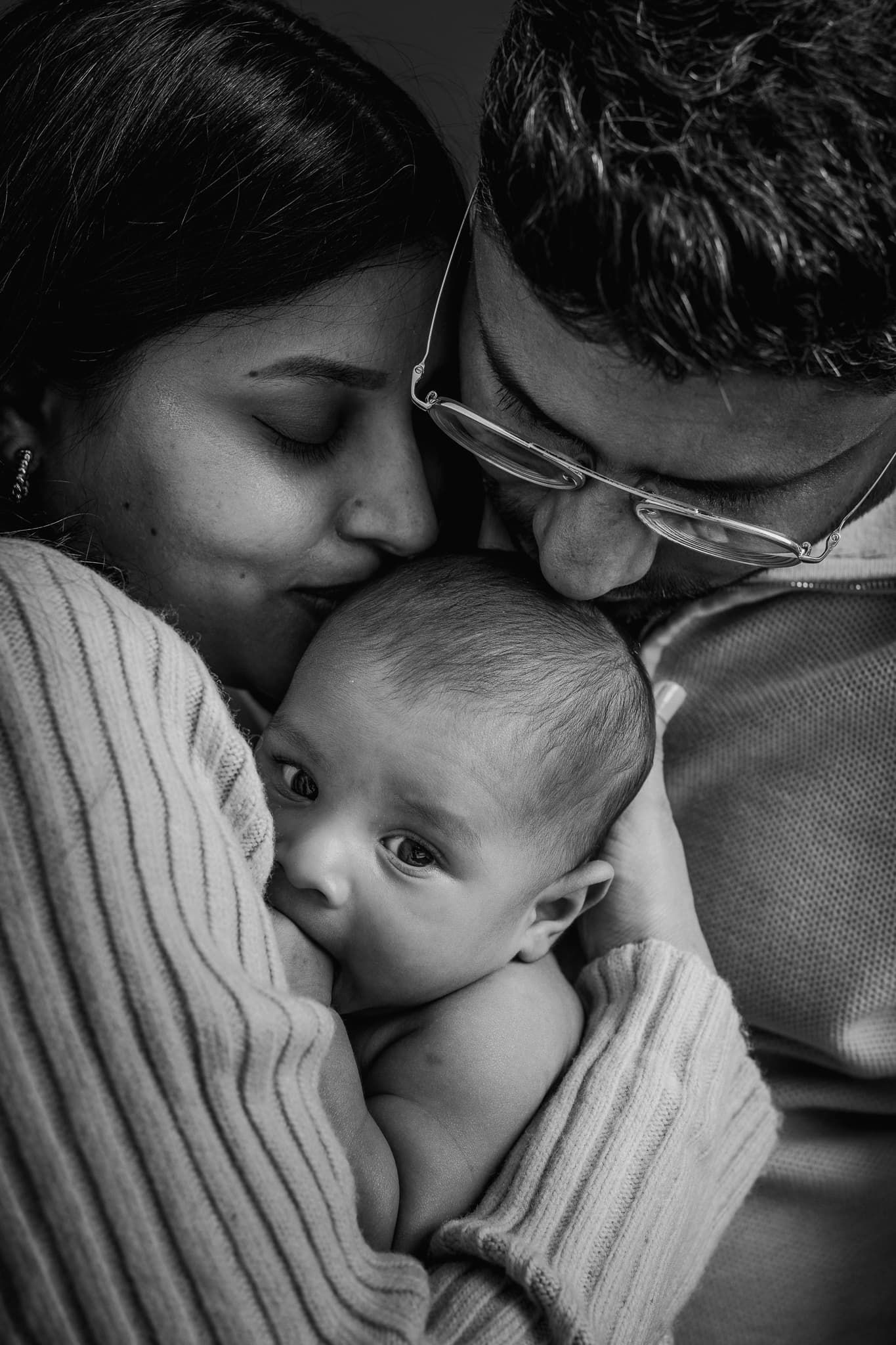 Mamma och pappa pussar sin nyfödda pojke på huvudet i fotostudio i Mullsjö Jönköping. Bilden är svartvit.