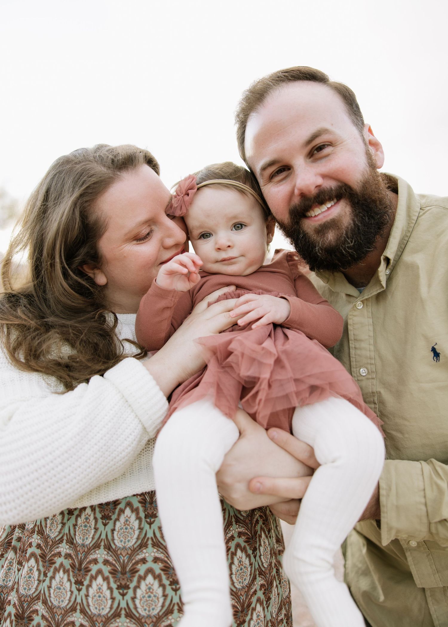 Happy family moment with baby in pink dress against white background.
