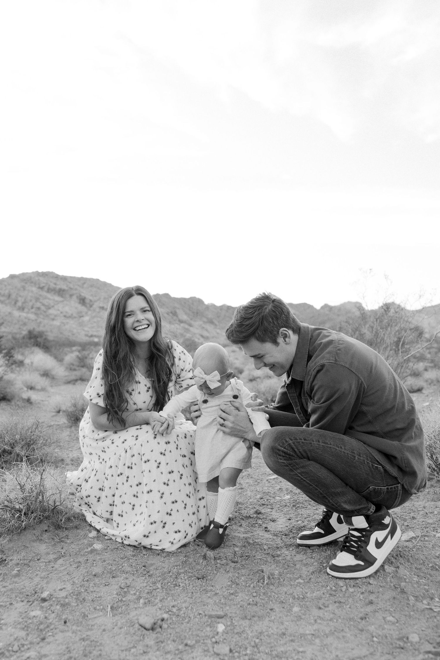 A series of black and white photos showing a family interacting with a small baby in an outdoor desert setting.