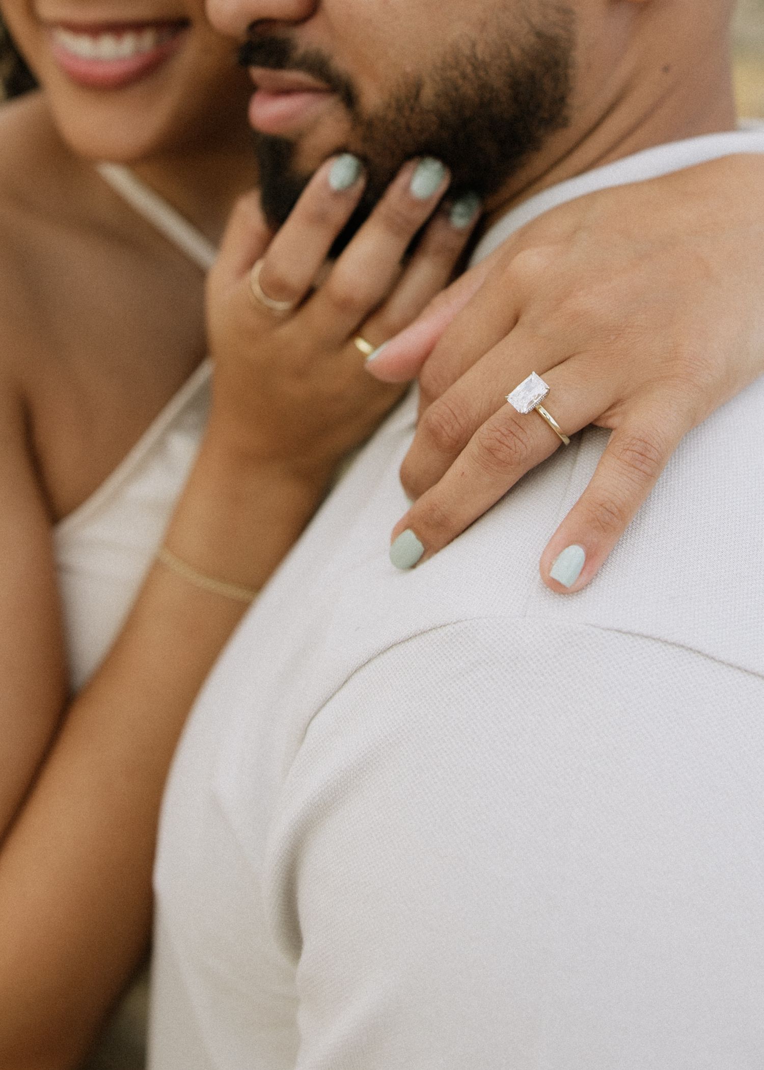 Close up of an engagement ring and painted nails as hands embrace.