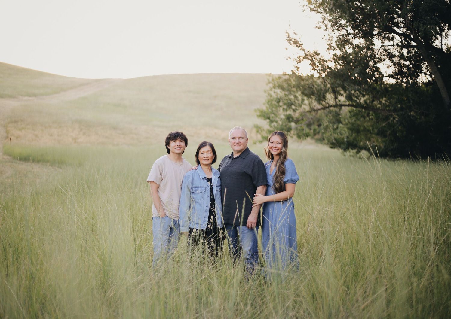 A group stands together in casual clothing among tall grass in a green hillside setting.