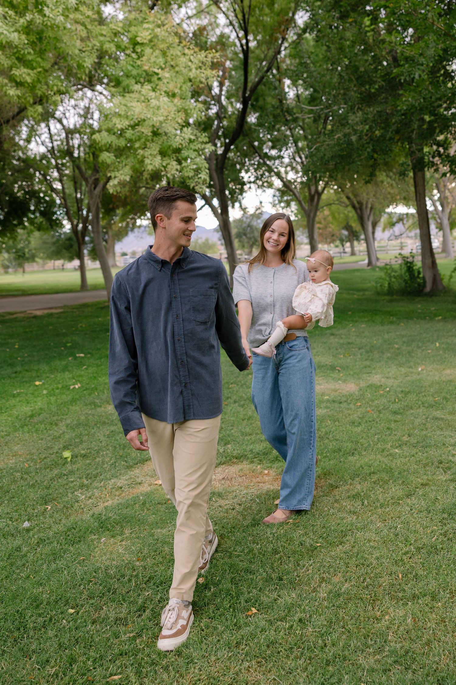 Family enjoying a playful moment together while walking on green grass in a park on a sunny day.