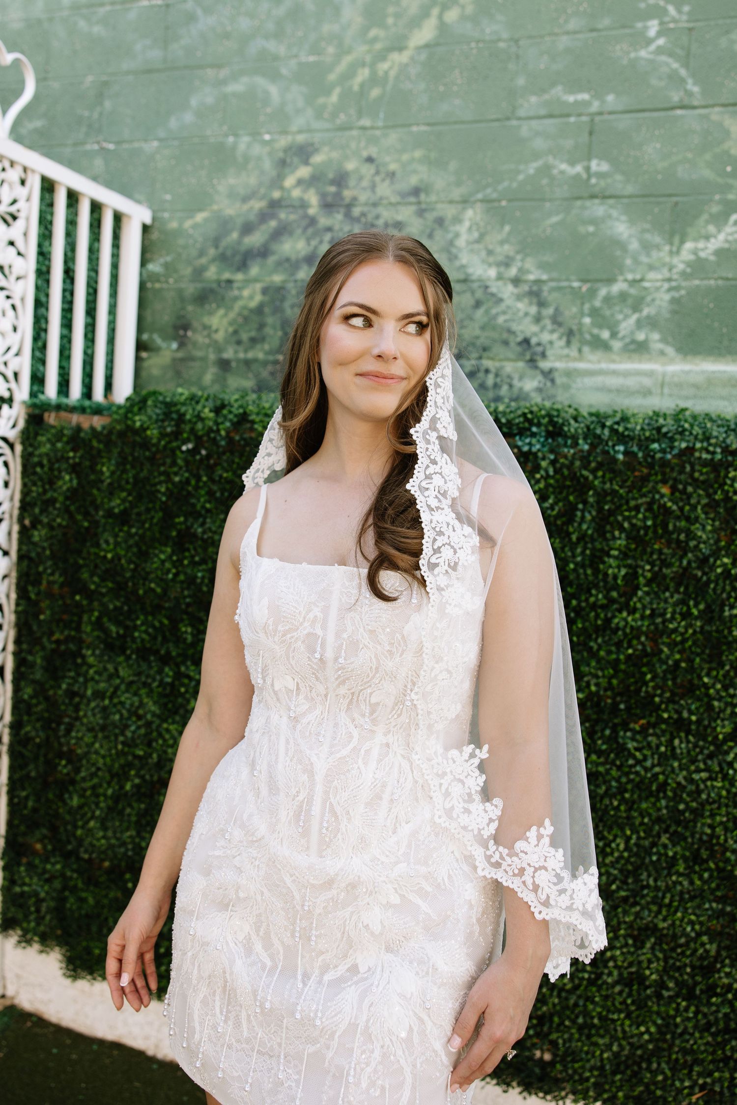 A bride in a white lace wedding dress poses against a green hedge backdrop in three similar photos.