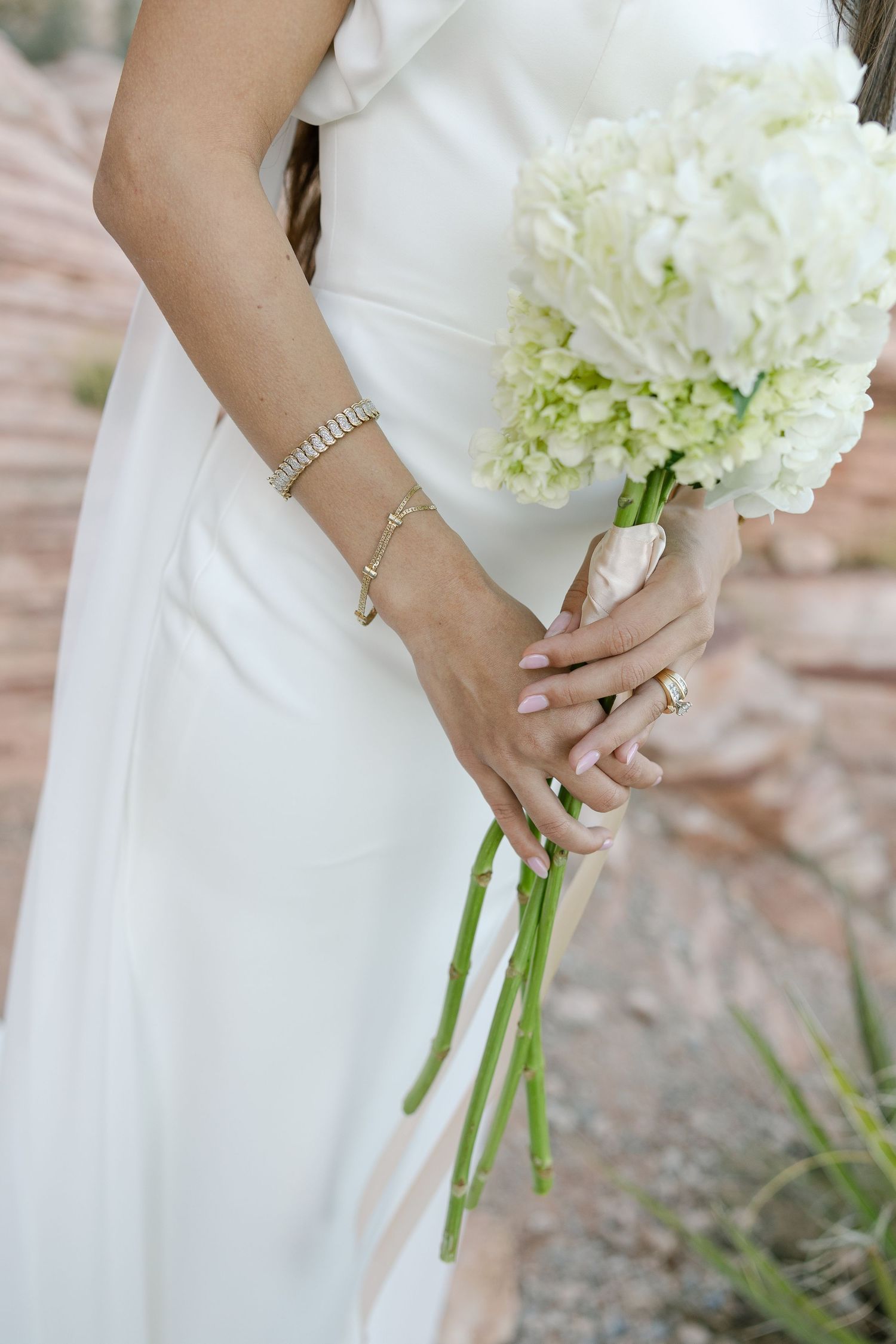 Close-up view of hands holding a white hydrangea bouquet while wearing a pearl bracelet and engagement ring.
