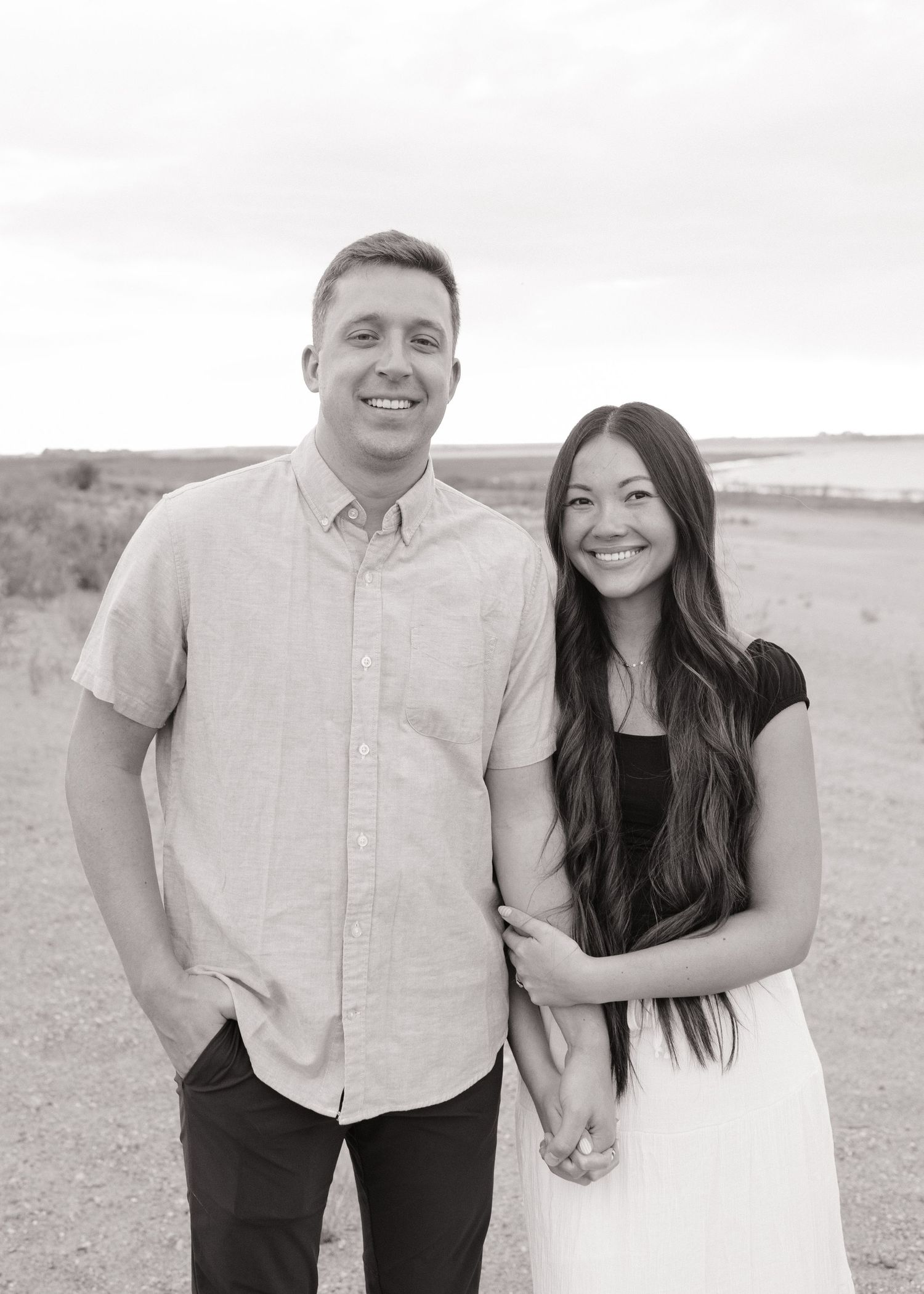 A couple poses together in casual attire against a desert landscape backdrop.
