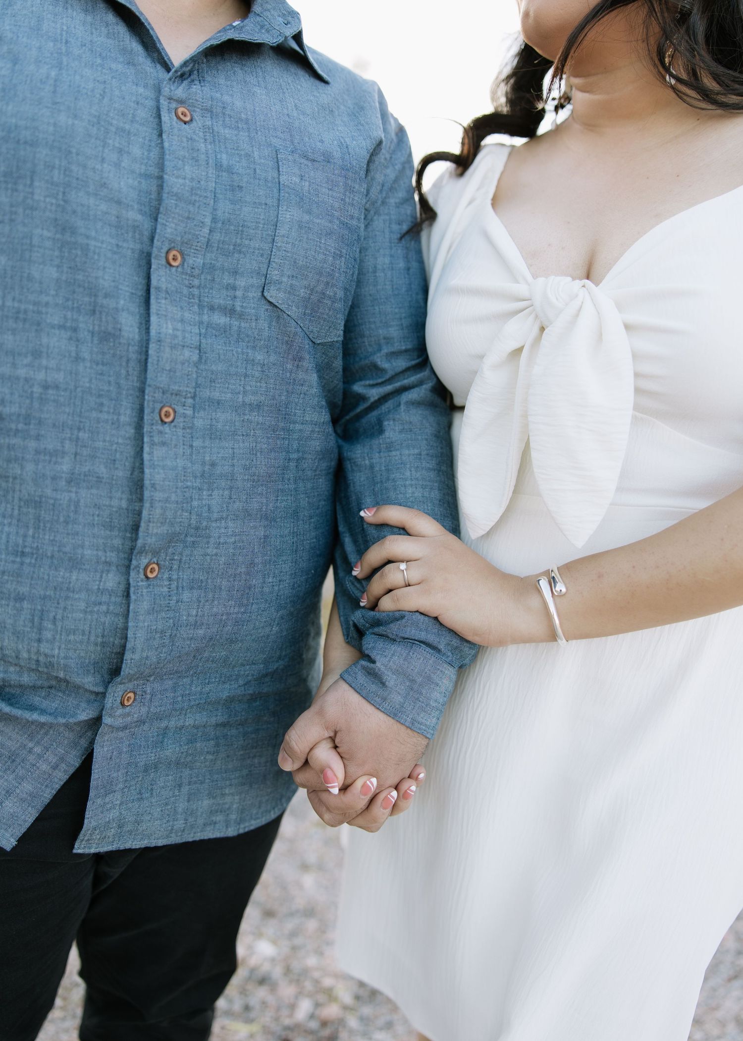 Close-up of couple holding hands, wearing blue linen shirt and white dress.