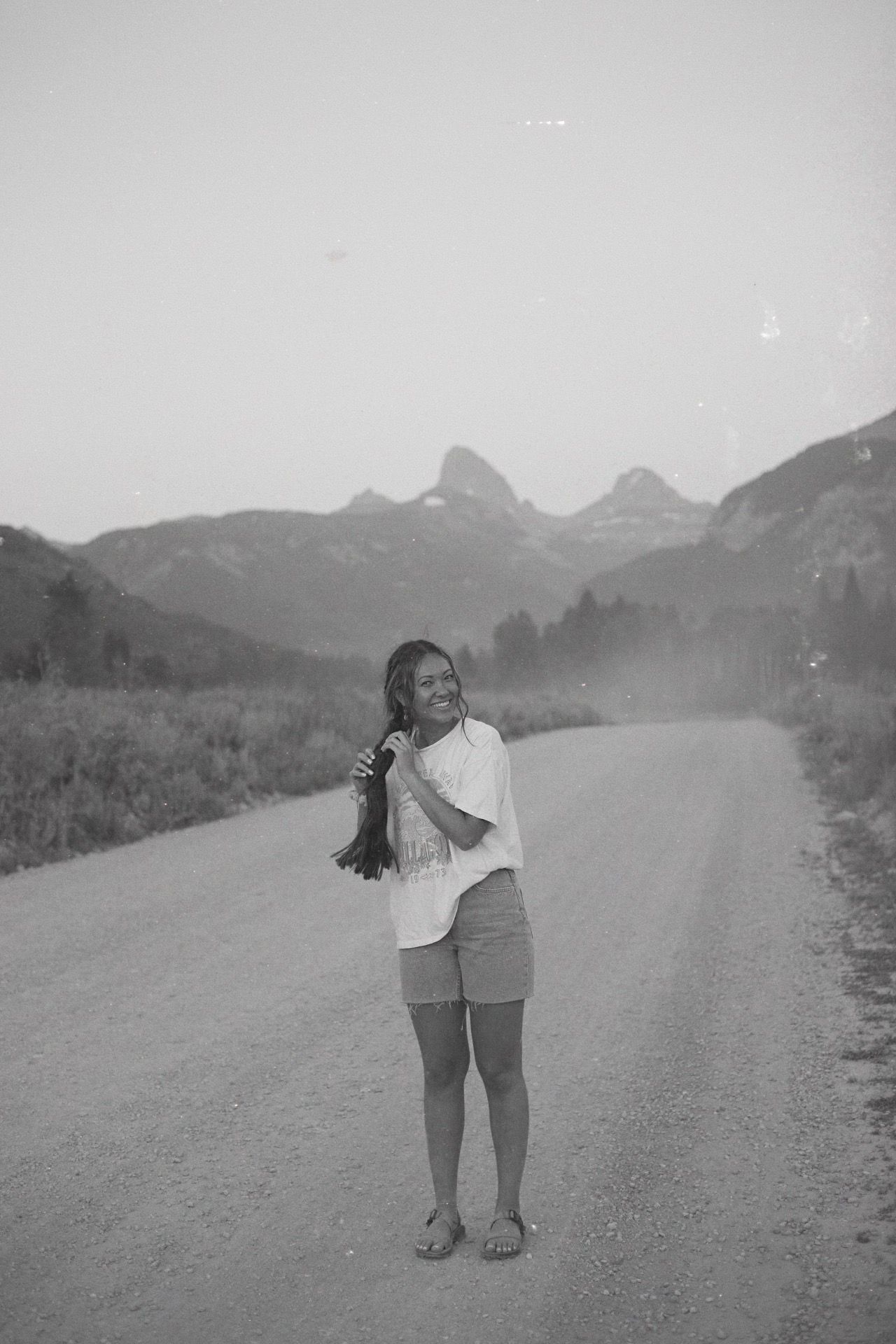 Black and white portrait on mountain dirt road with peaks in background.