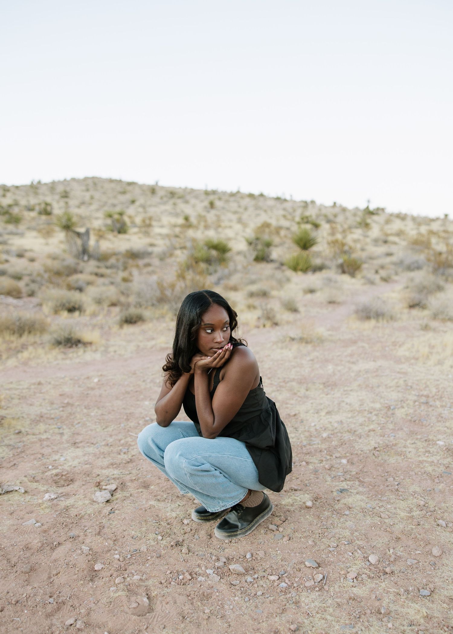 Person in casual attire crouching in an arid desert landscape.