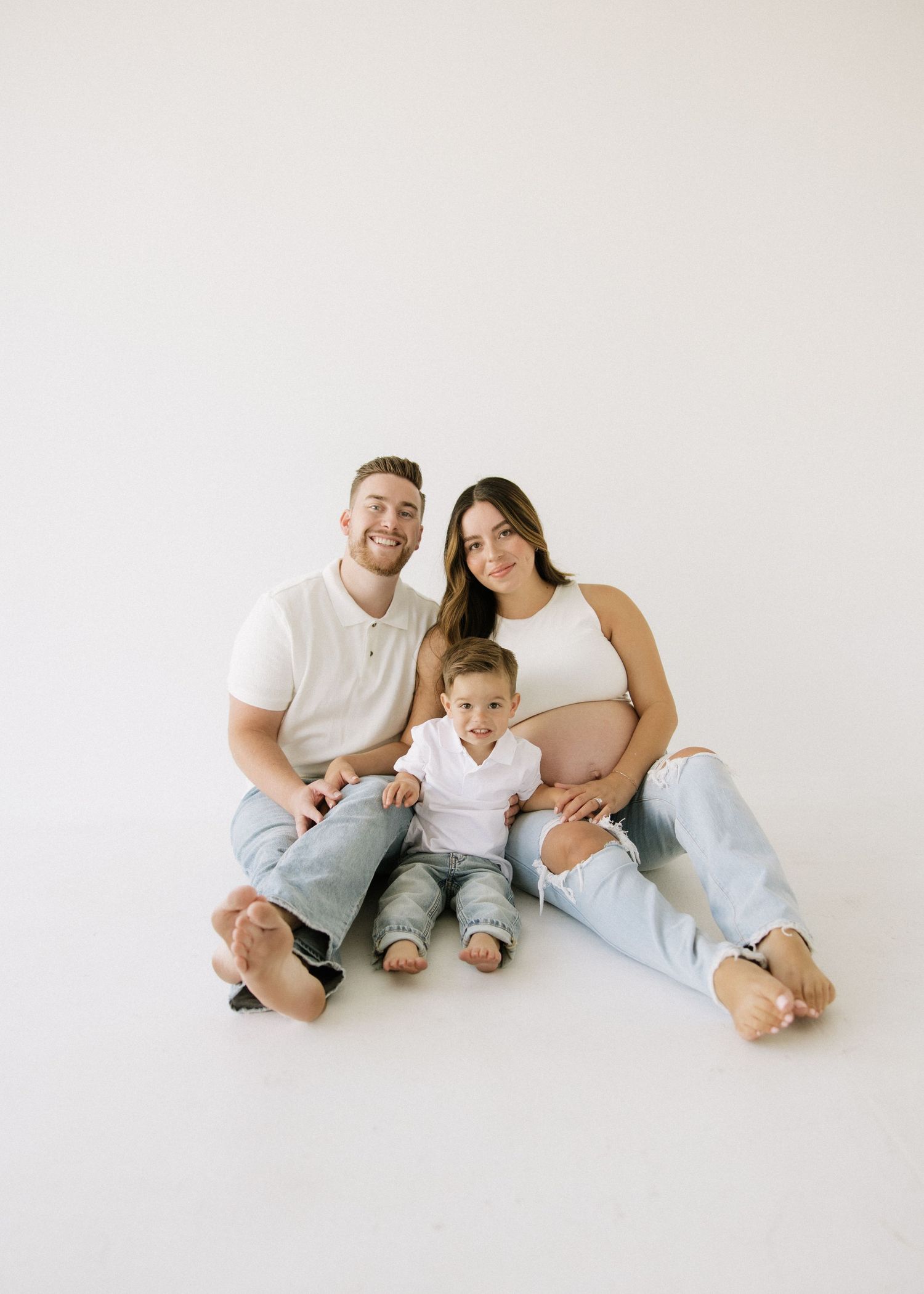 A family sitting together on the floor in a bright minimalist setting for a portrait session.