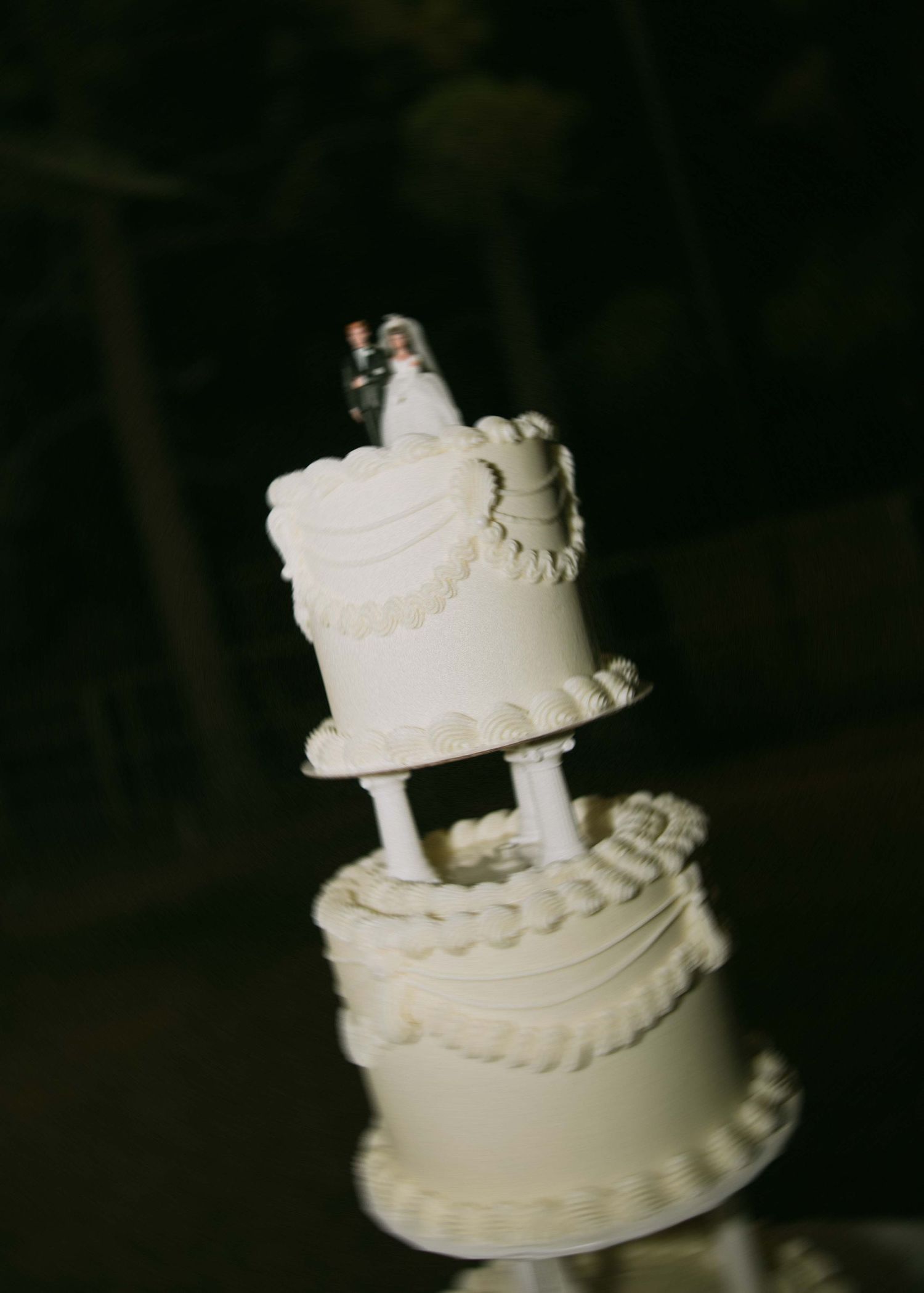 An elegant two-tiered white wedding cake with delicate piping and a miniature bride and groom topper.