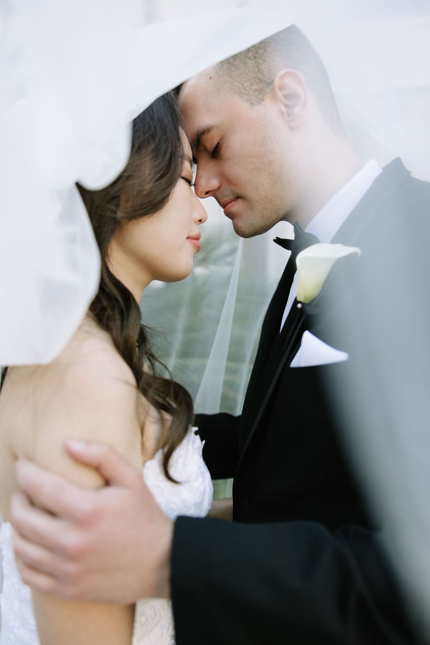 Romantic close-up portrait of newlyweds sharing an intimate moment under a sheer veil.
