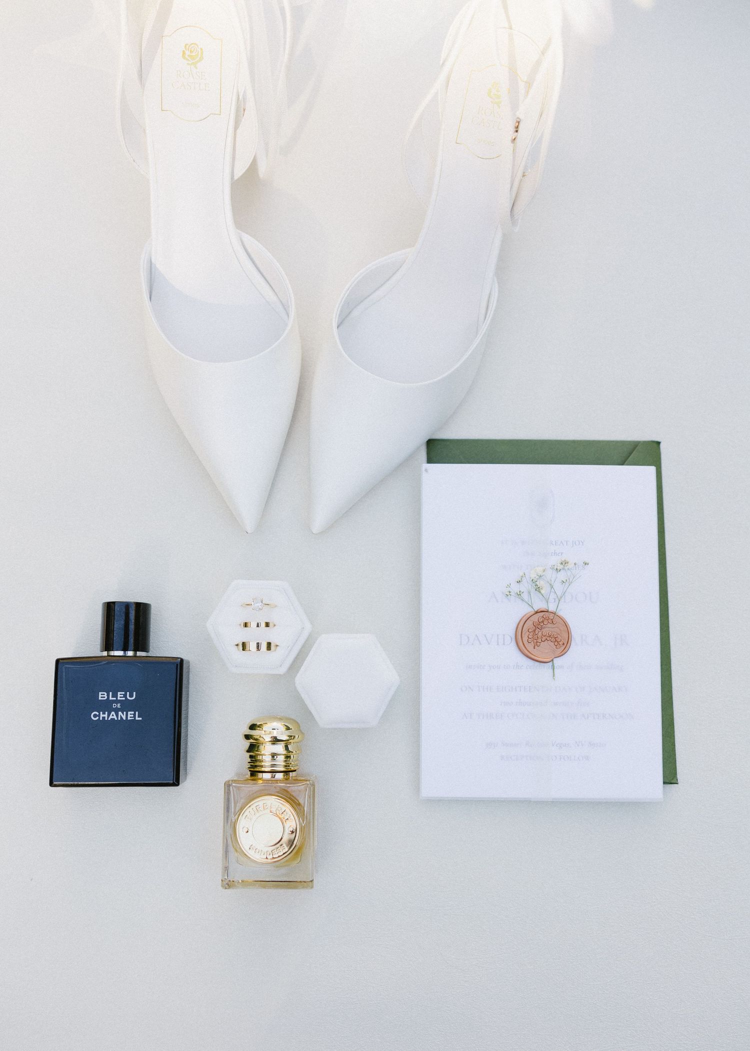 Flat lay of white bridal shoes, perfume bottles, and wedding invitation with wax seal.