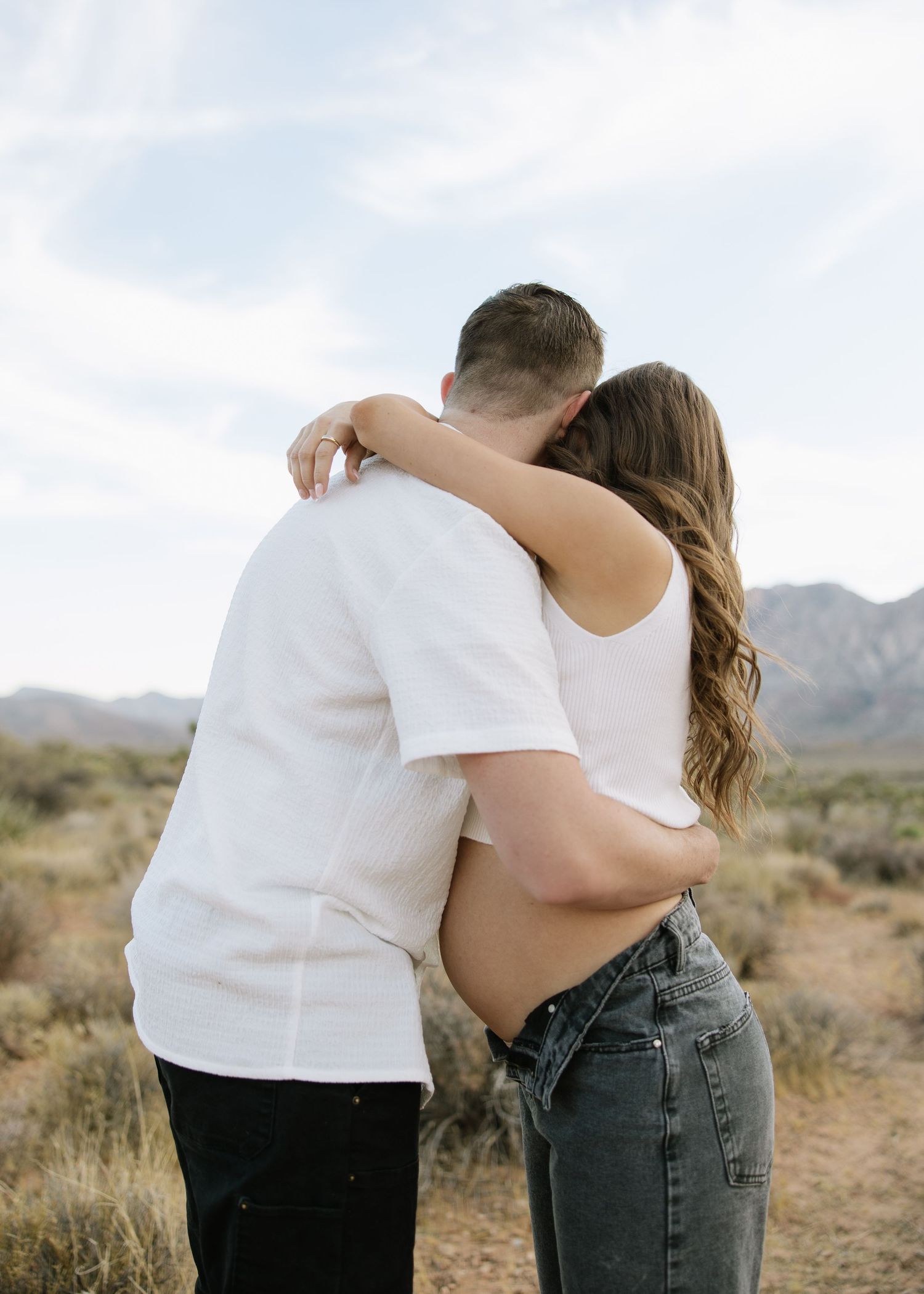 Couple embracing on desert trail with mountains in background.
