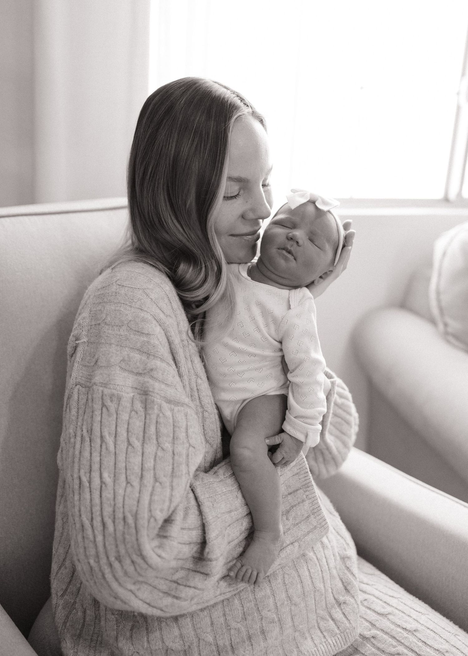 A tender moment between parent and baby in cozy sweaters on a white sofa.