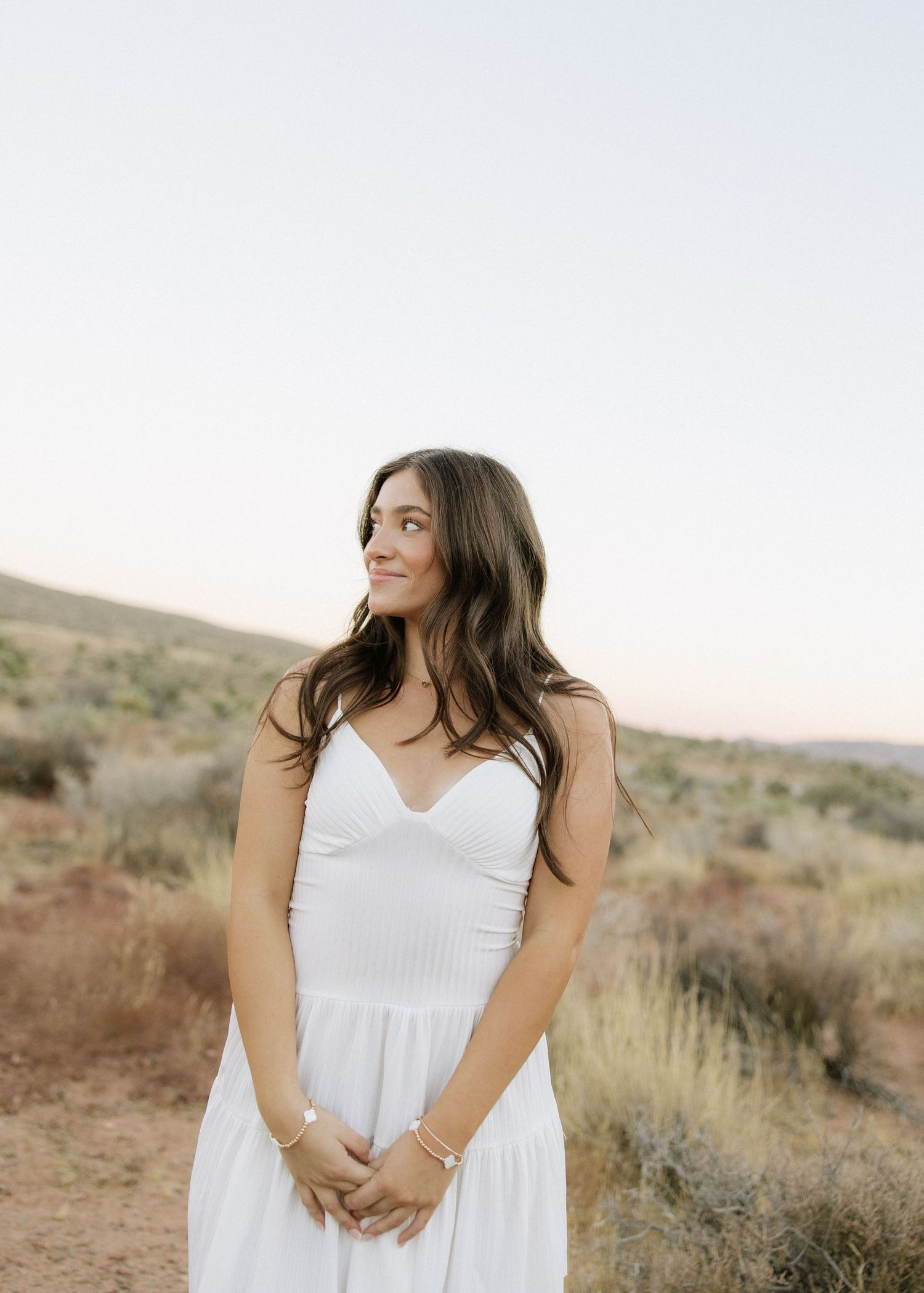Portrait in desert landscape with mountains and brush in background.