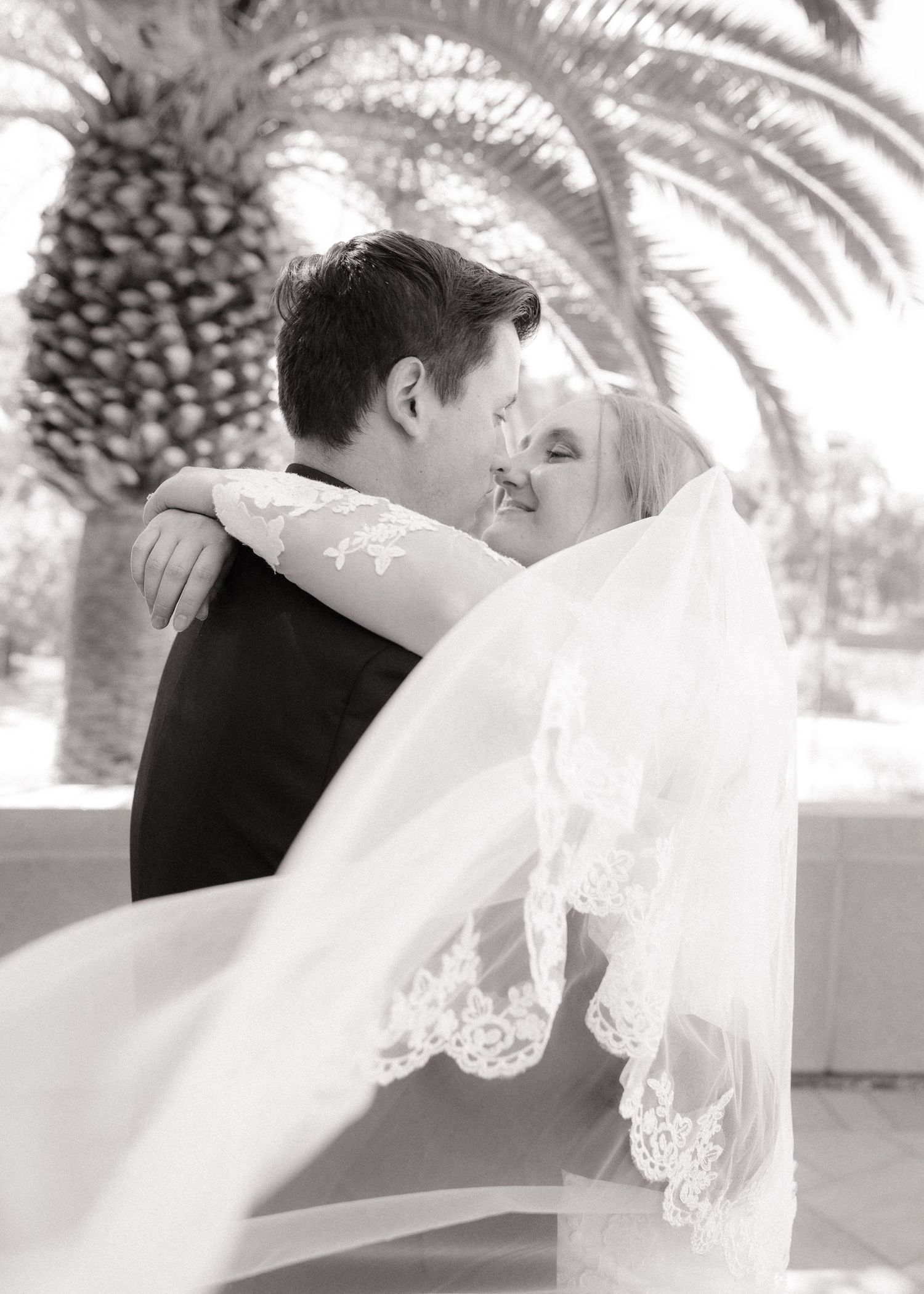Tender wedding moment captured in black and white with bride's veil flowing in breeze.