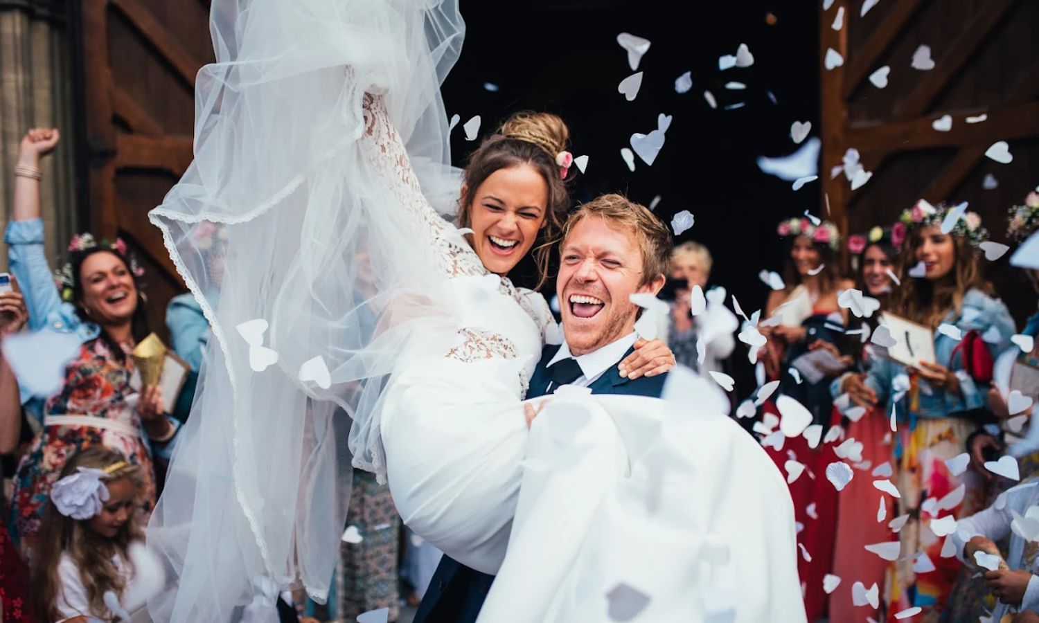 Wedding guests throw white confetti as newlyweds celebrate outside during a joyous ceremony exit.