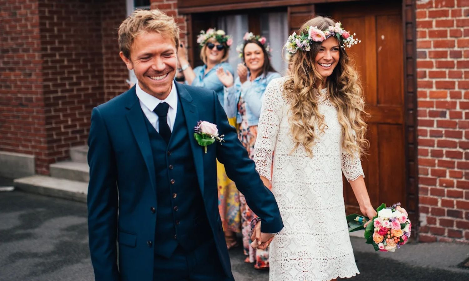 A bride and father share a joyful moment together during a wedding ceremony outside a brick building.