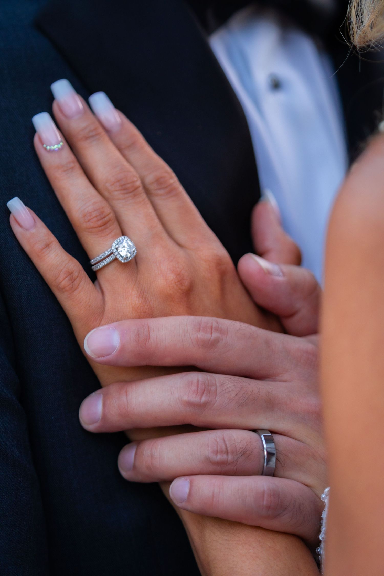 Close-up of bride and groom hands showing diamond engagement ring, wedding band, and groom's silver ring.