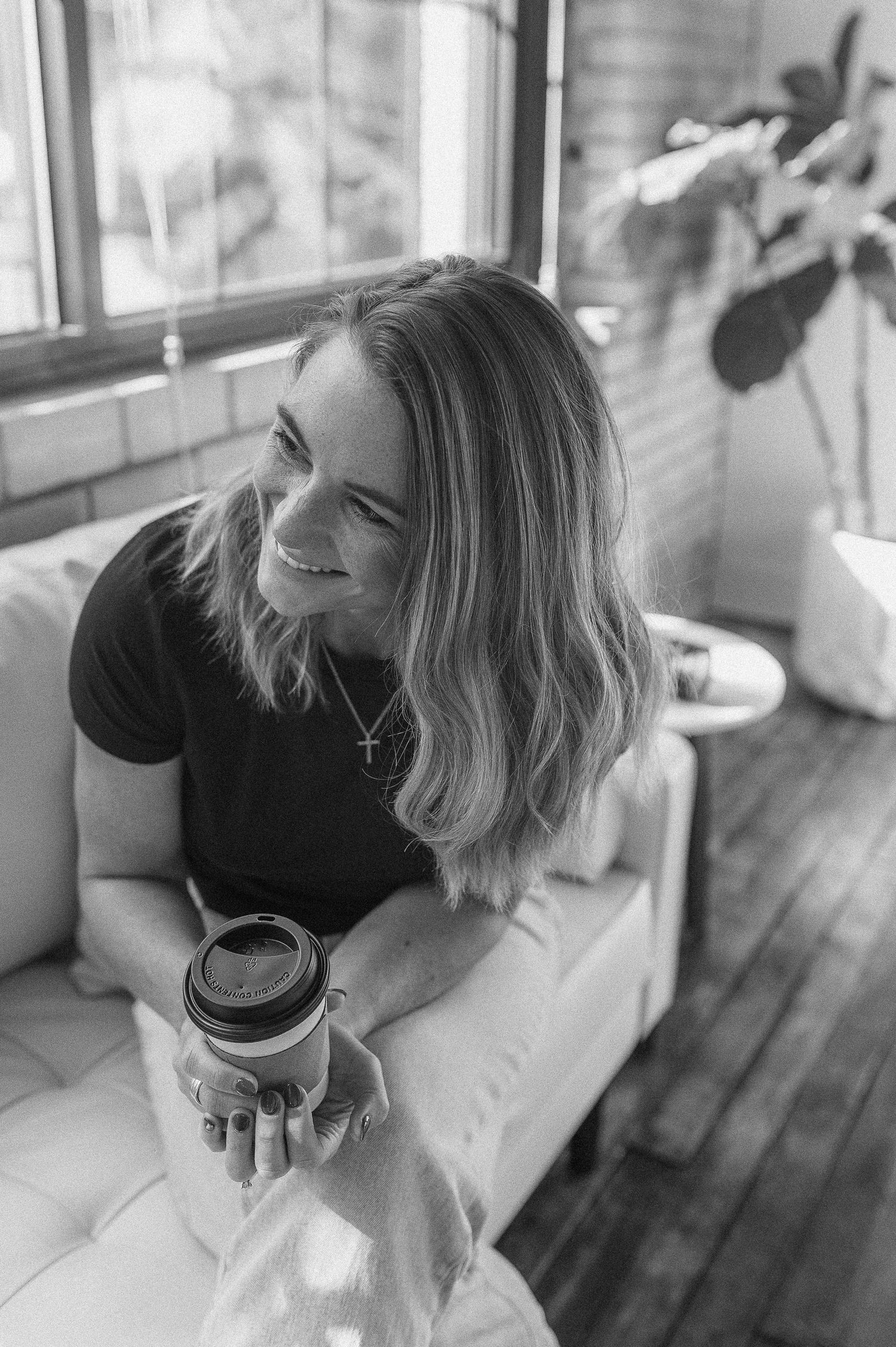 A black and white candid portrait of someone smiling while holding a coffee cup.