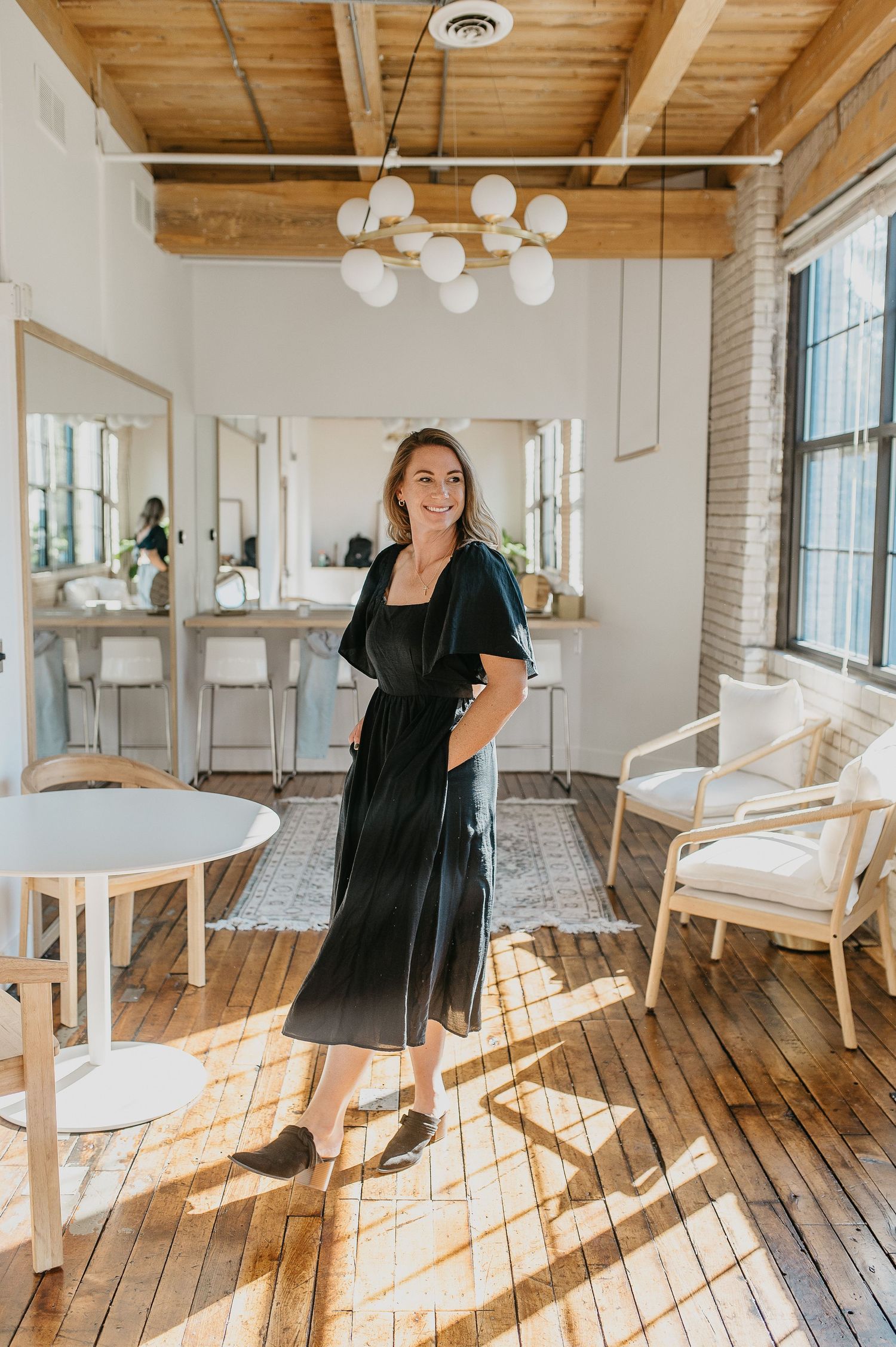 A bright modern salon space with wooden floors, white walls, and globe pendant lighting.