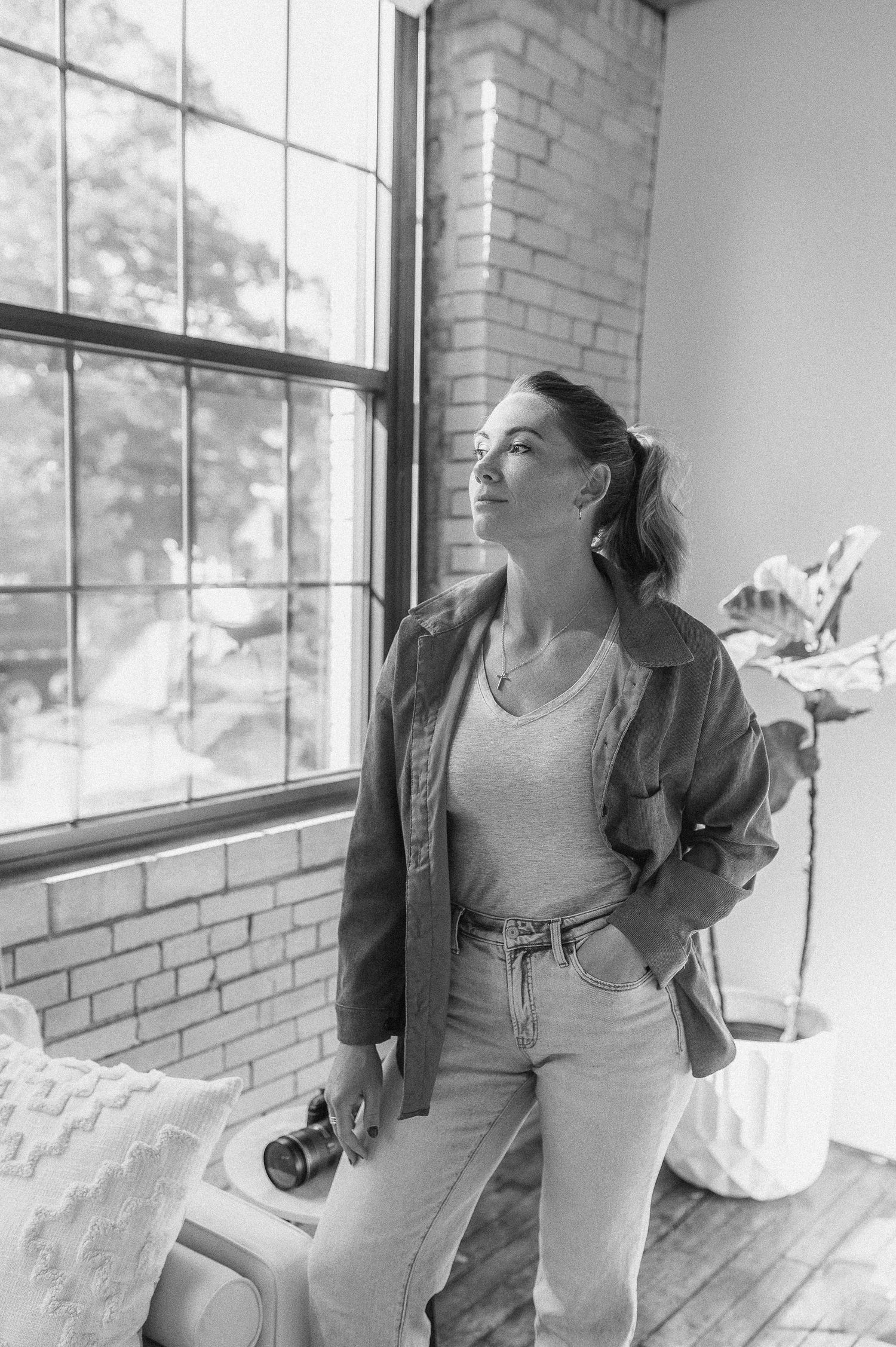 A black and white portrait by a brick window in an industrial style space.