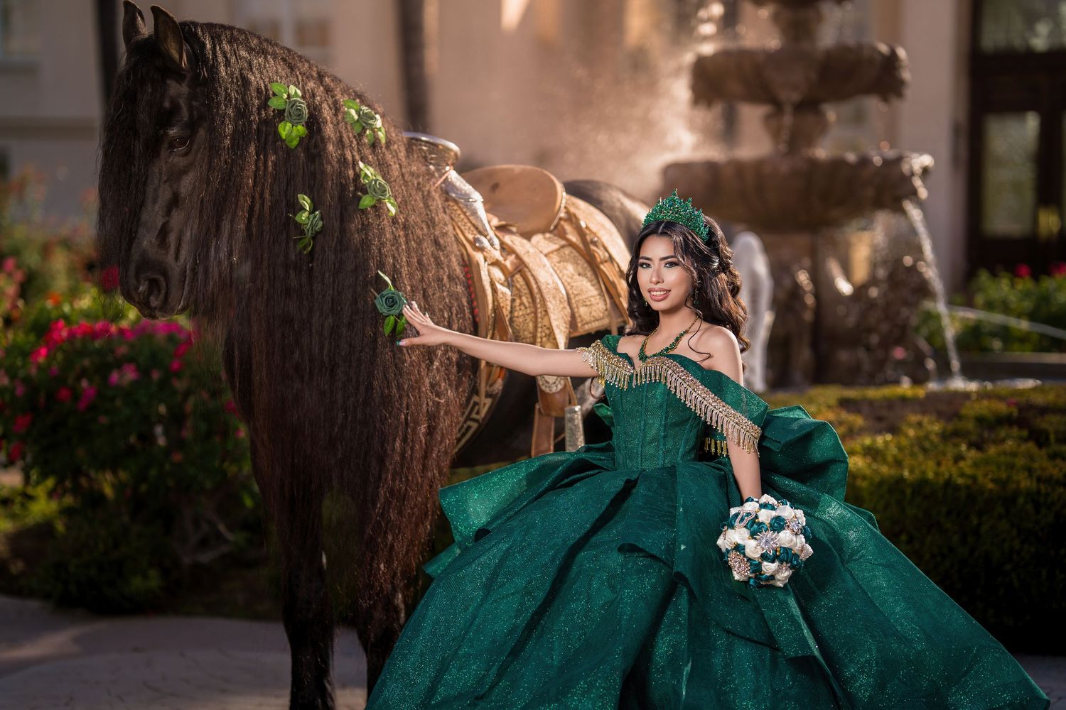 Young woman in emerald green quinceañera ball gown poses beside a horse near a fountain outdoors.