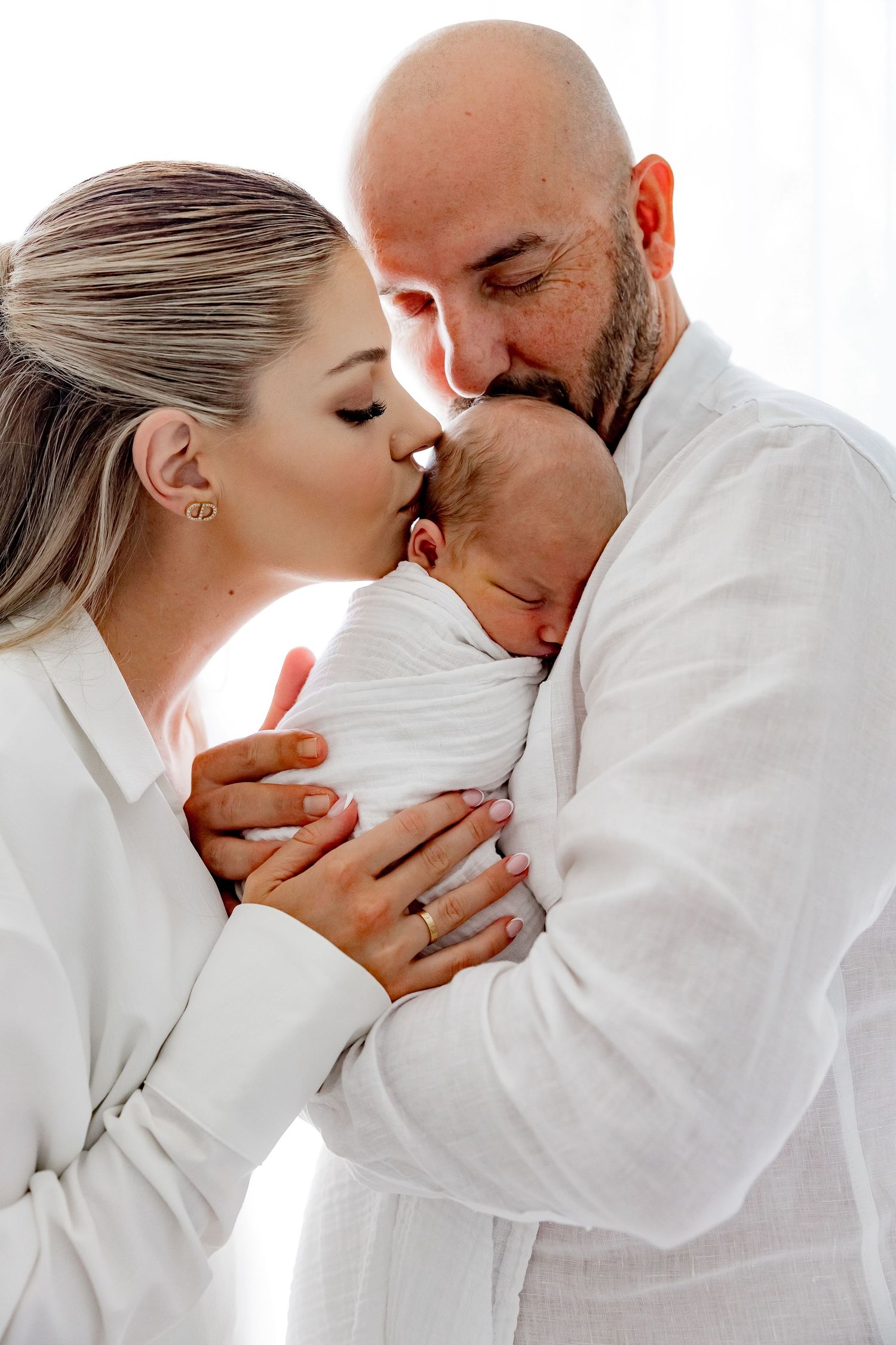 Romantic couple in white clothing sharing intimate moments in a bright minimalist setting.