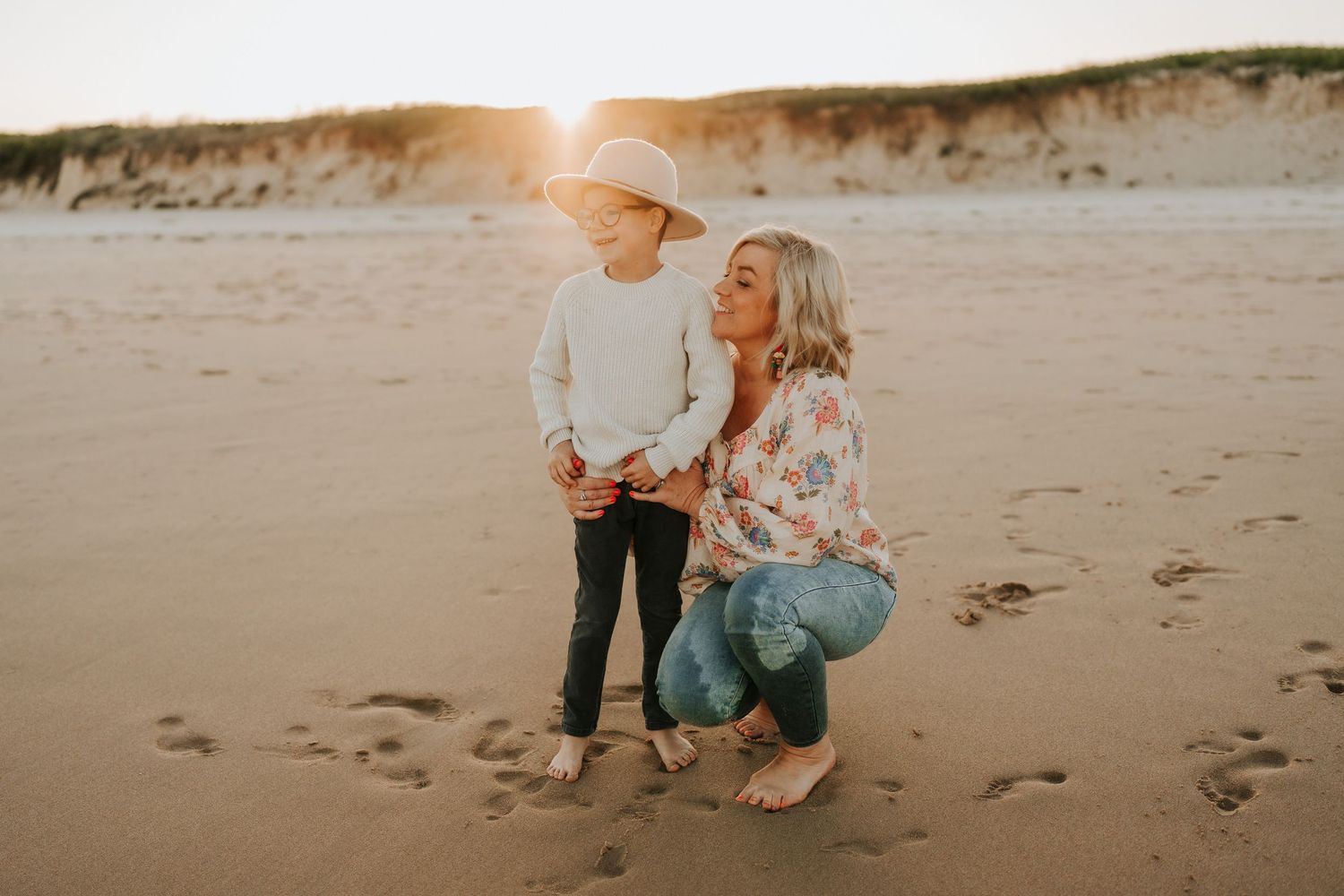 A sunset beach photoshoot with two people posing on sandy shores at dusk.