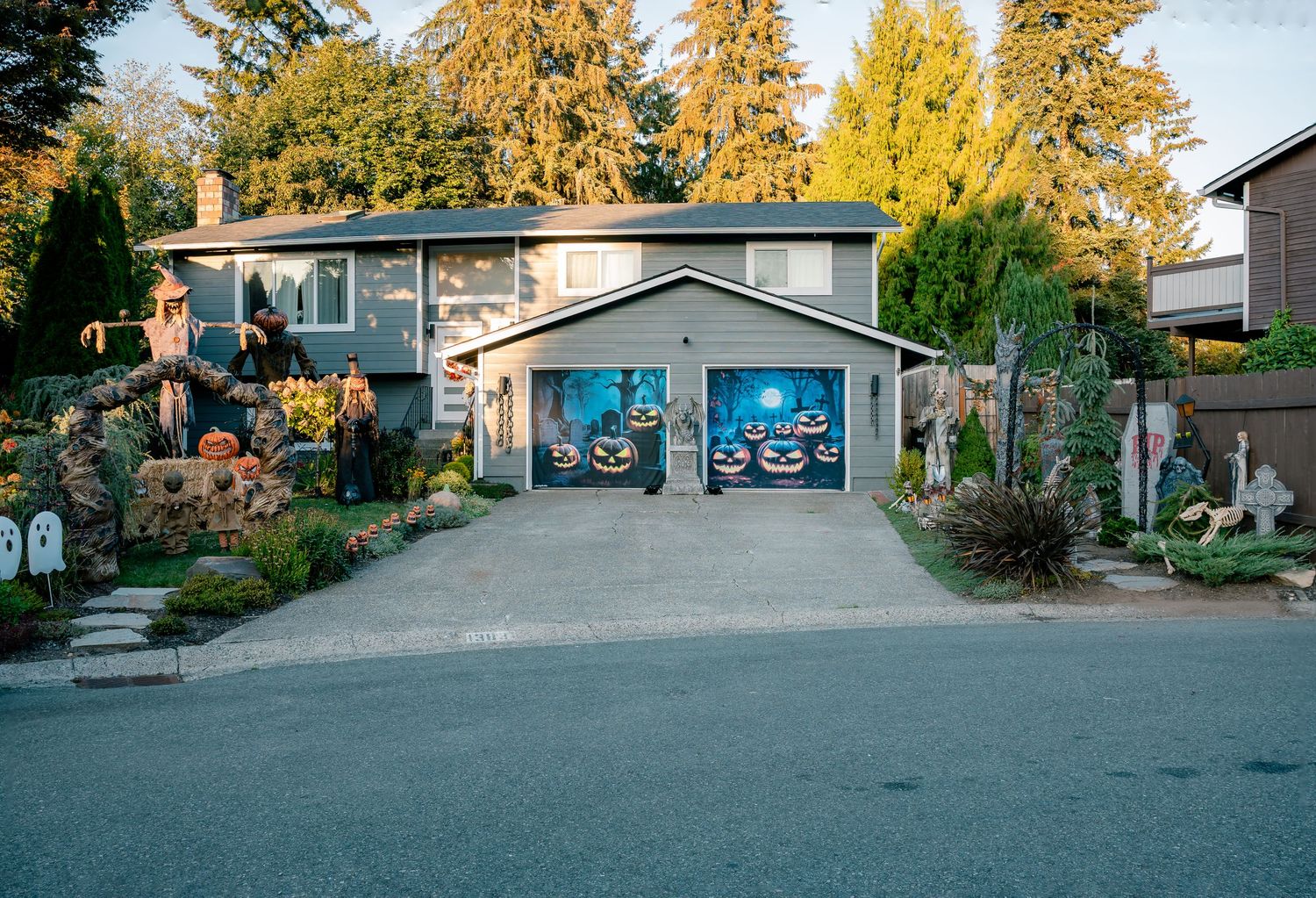 Halloween-decorated suburban house with spooky garage door murals, pumpkins, and festive yard decorations.