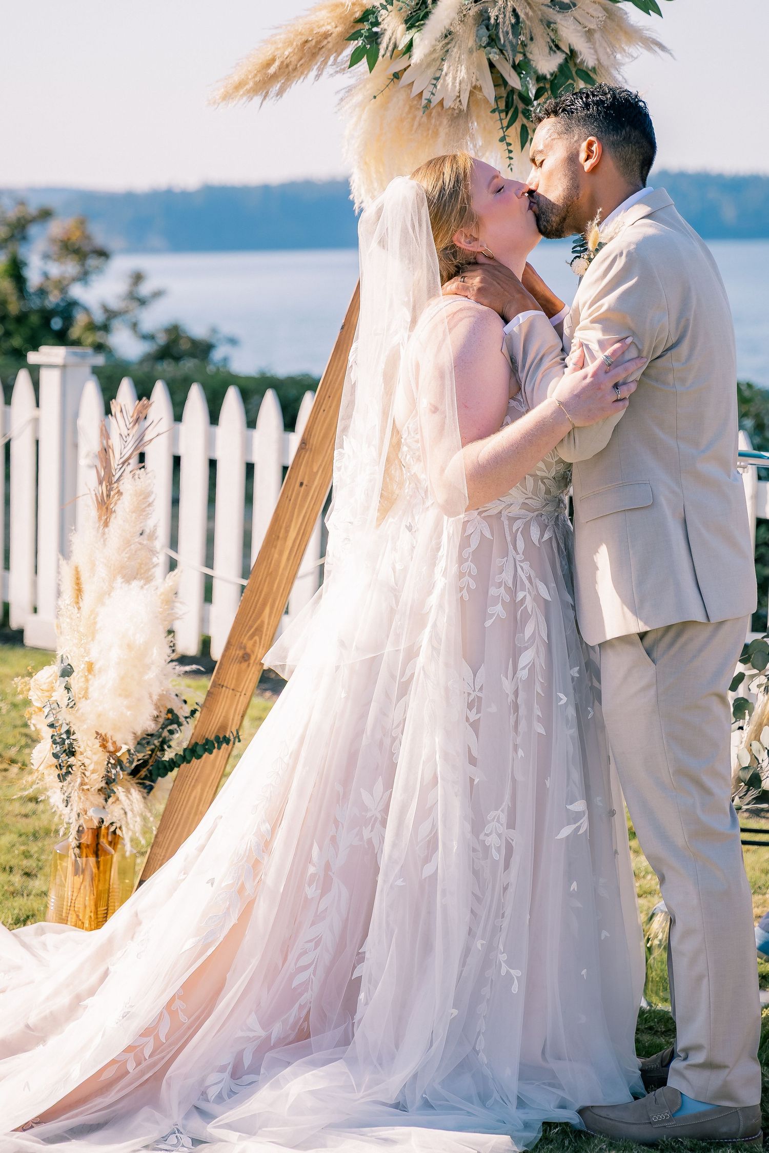Bride and groom share a first kiss at a boho outdoor wedding ceremony by the water.