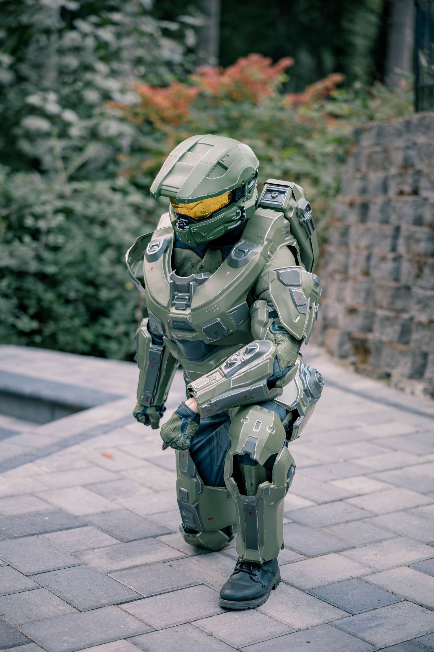 Full Halo Master Chief cosplay costume with green armor and yellow visor walking on a brick pathway.