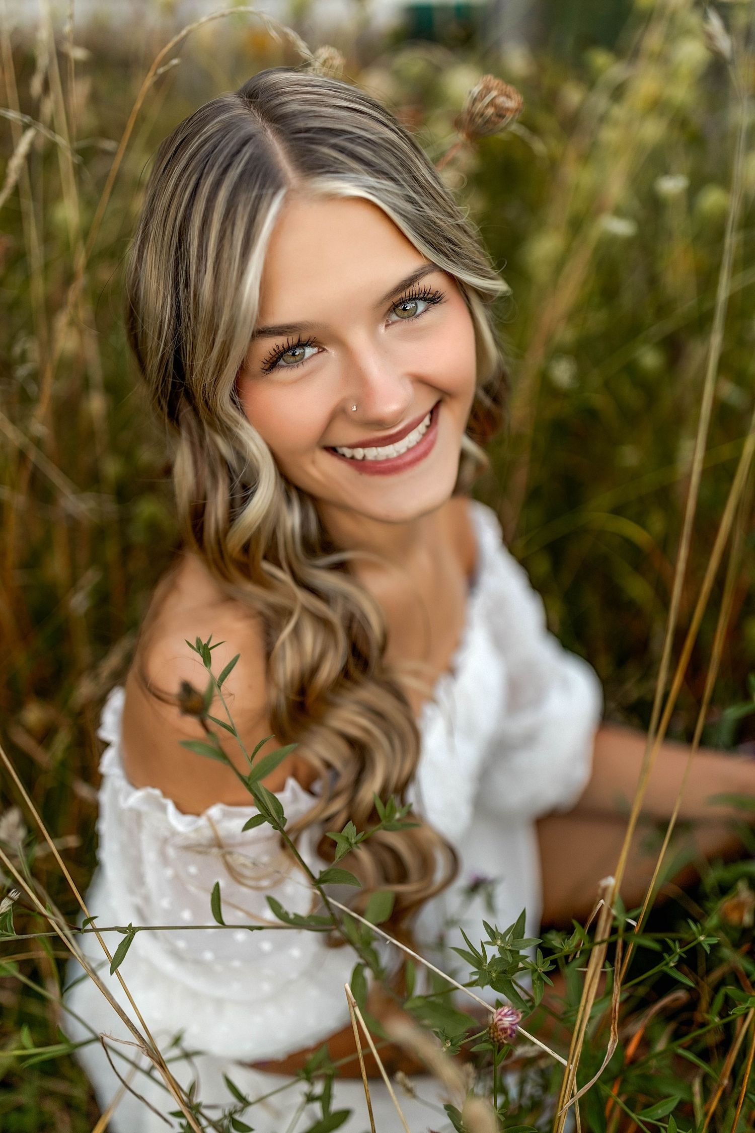 Senior girl in white dress squatting in a field of flowers and greenery