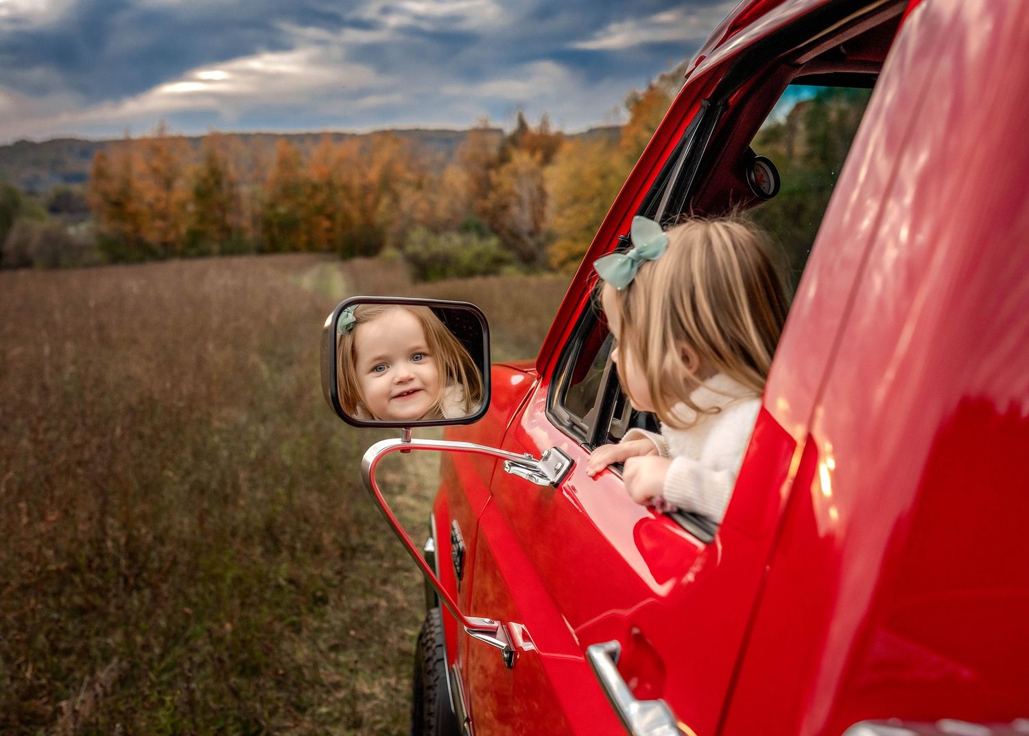 Child sitting in truck leaning out the window and looking in the mirror in Central NY