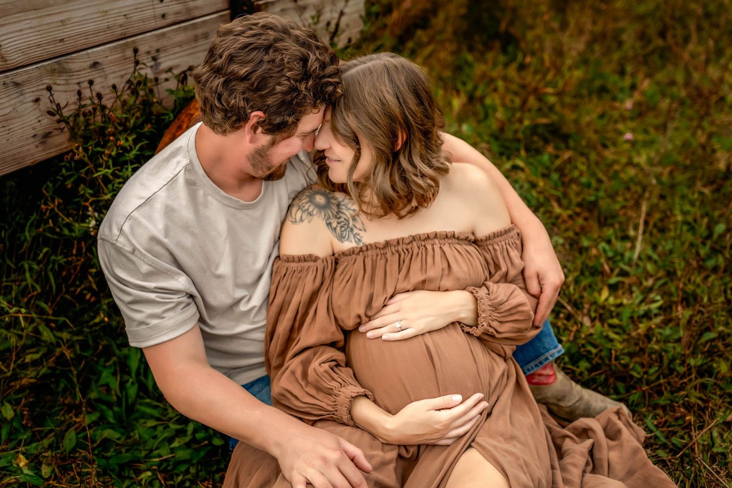 Couple maternity photos sitting on the ground in a green field in Central NY