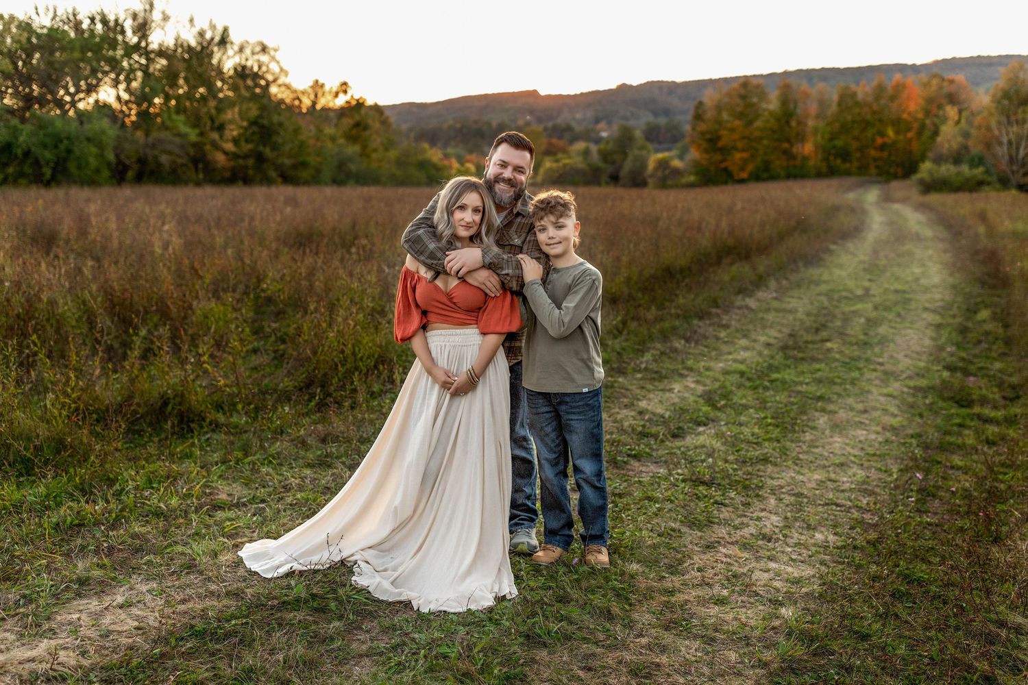 Family of 3 hugging for family photo in a field in Central NY