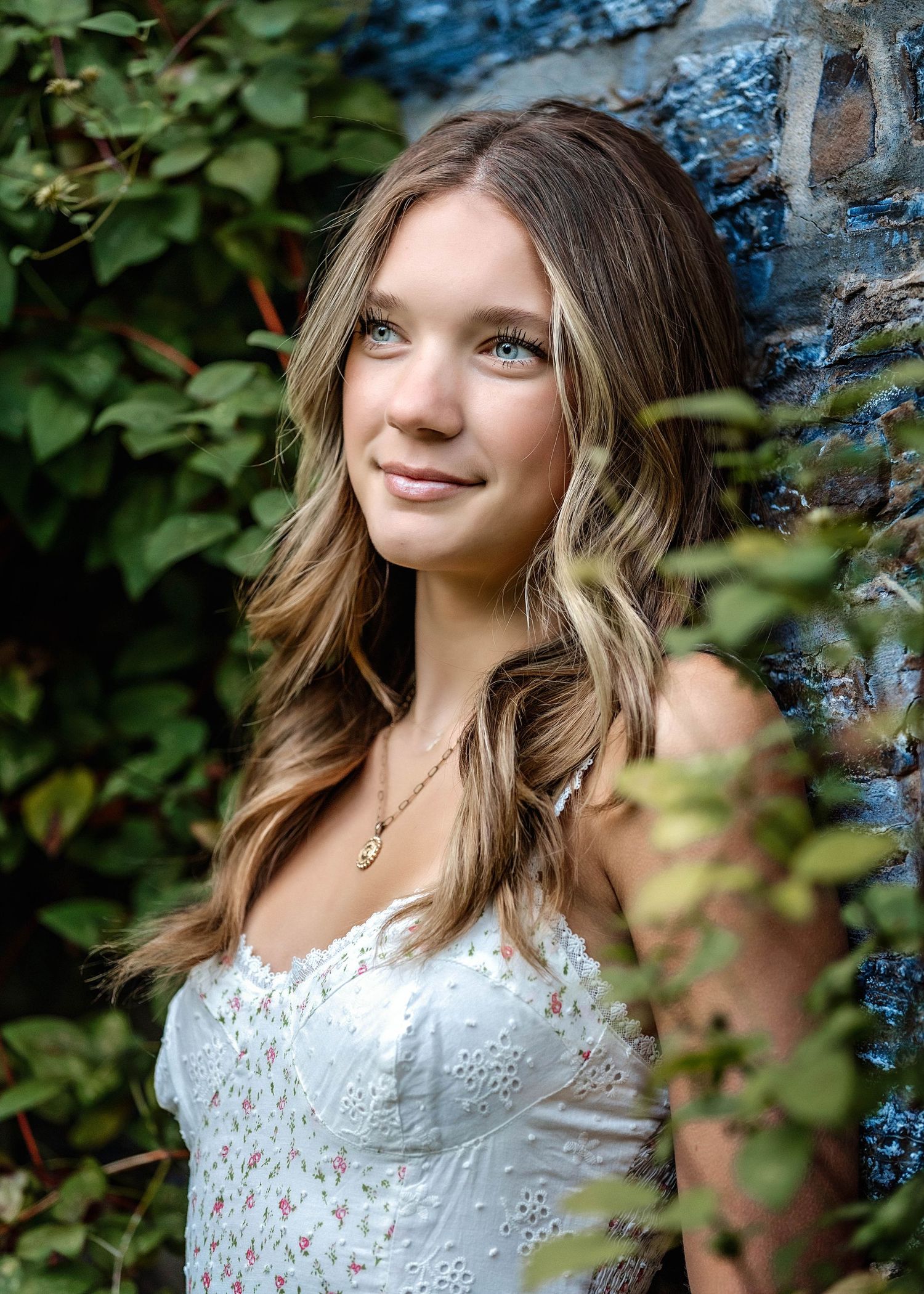 Senior girl leaning against a stone wall wearing a white floral dress in Central NY