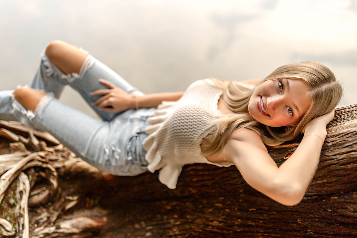 Senior girl laying on fallen tree trunk in front of a lake in Central NY