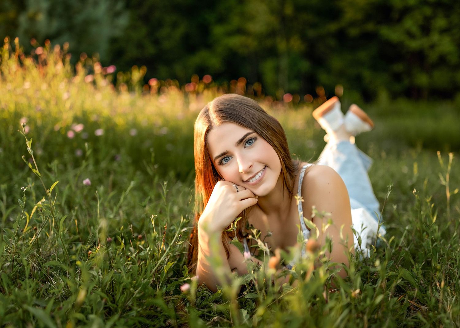 Senior girl laying on her stomach leaning her chin on her hand in a green field in Central NY