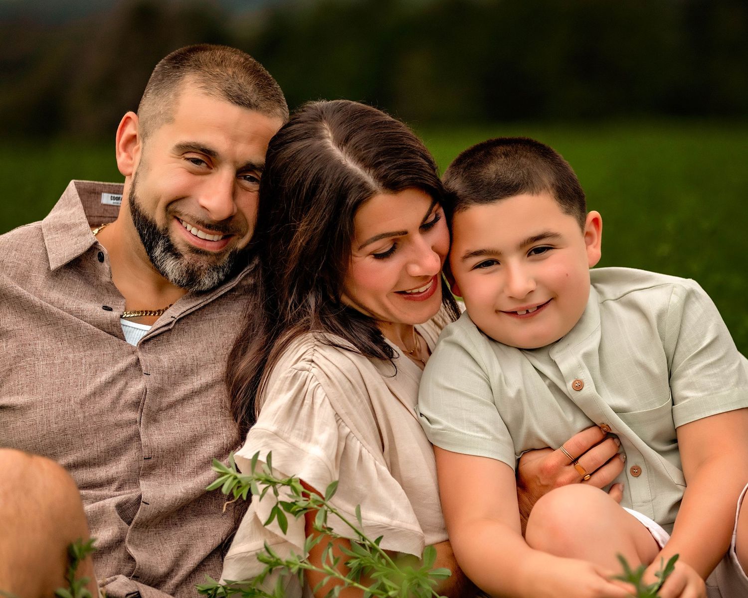 Parents and child sitting on the ground together and hugging in a field in Central NY