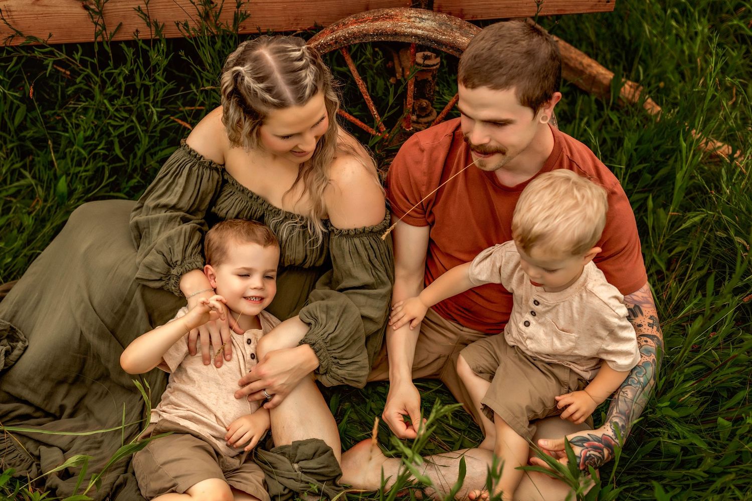 Styled family sitting by each other on the ground in front of a wagon in a field in Central NY